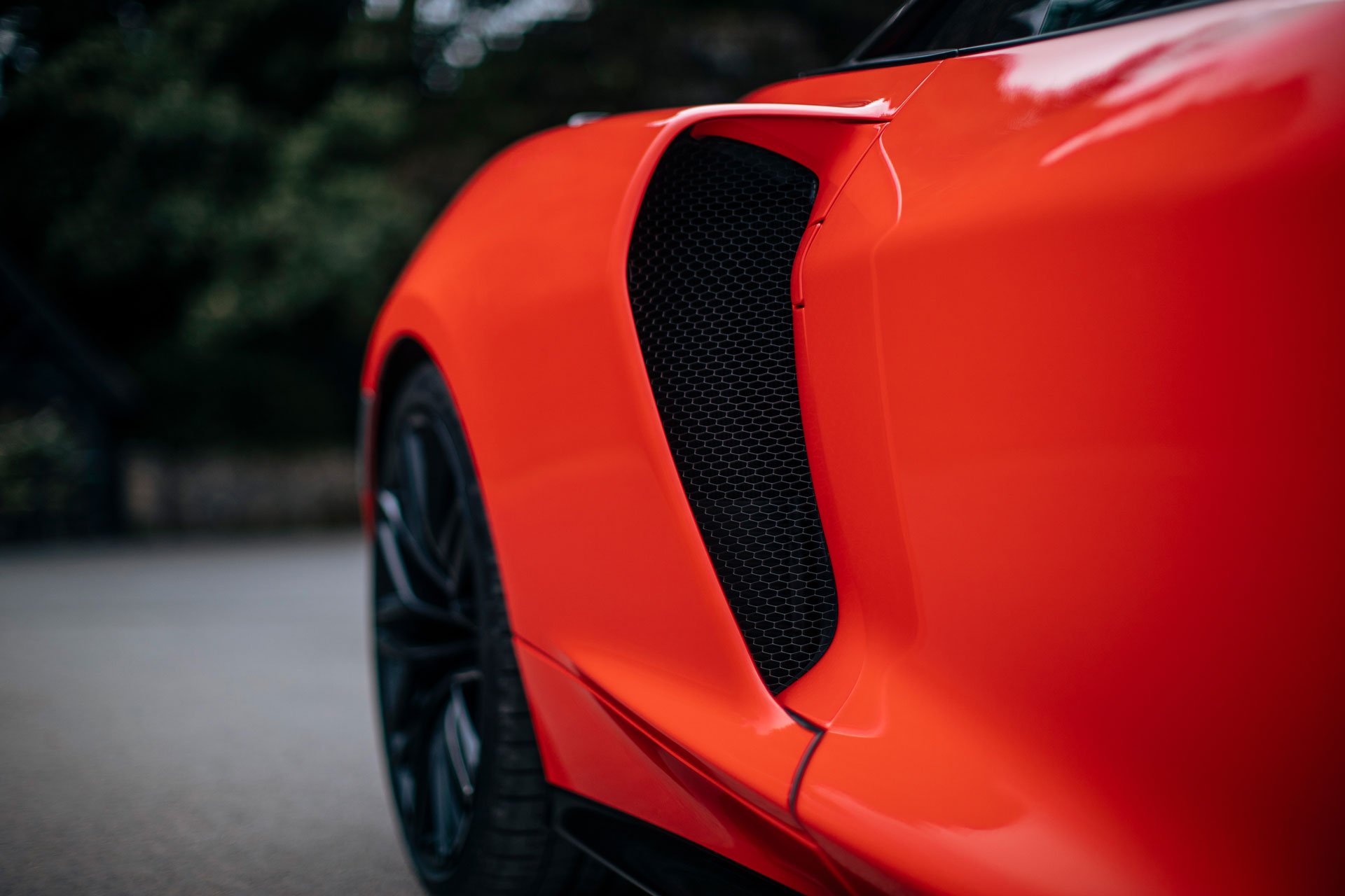 A close-up, low-angle shot highlighting the side air intake and rear wheel of a bright red McLaren GTS.