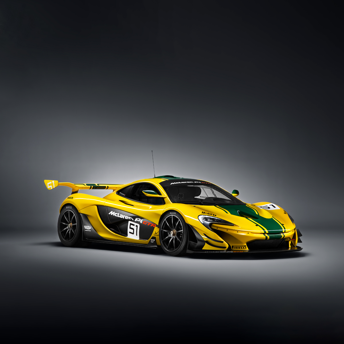 Side view of a yellow McLaren P1 GTR with green racing stripe, number 51, and sponsorship advertising on the body, photographed in a grey studio environment.