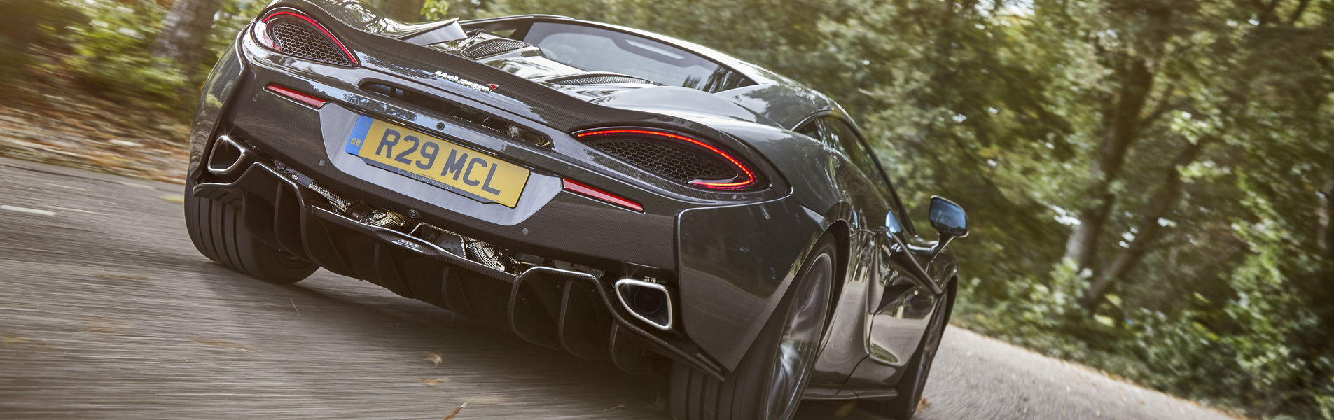  A low-angle action shot of a dark grey McLaren sports car, driving away