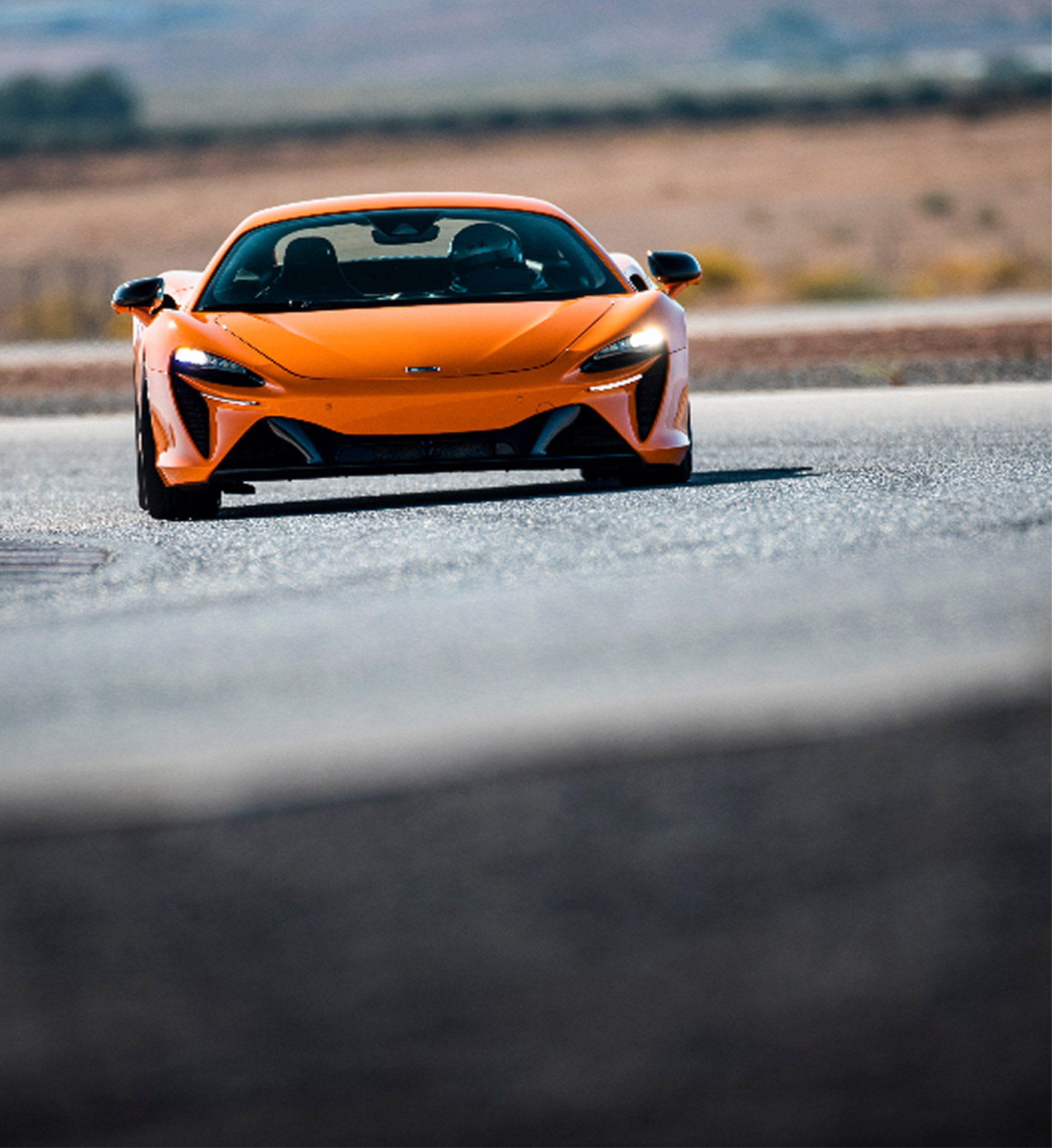 Orange McLaren Artura driving on a track.