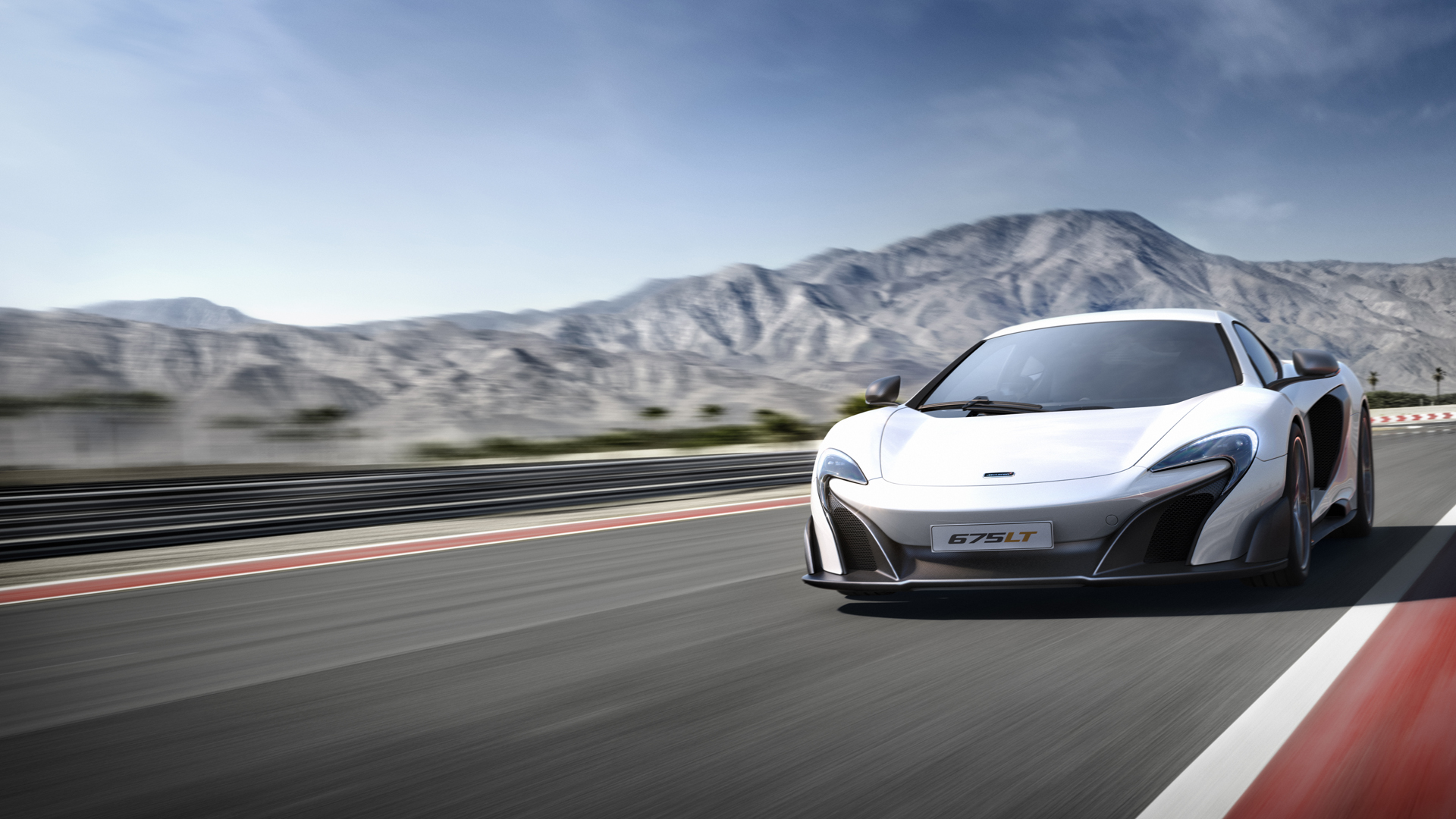 A white McLaren 675LT driving down a road at speed. Blurry mountains can be seen in the background.