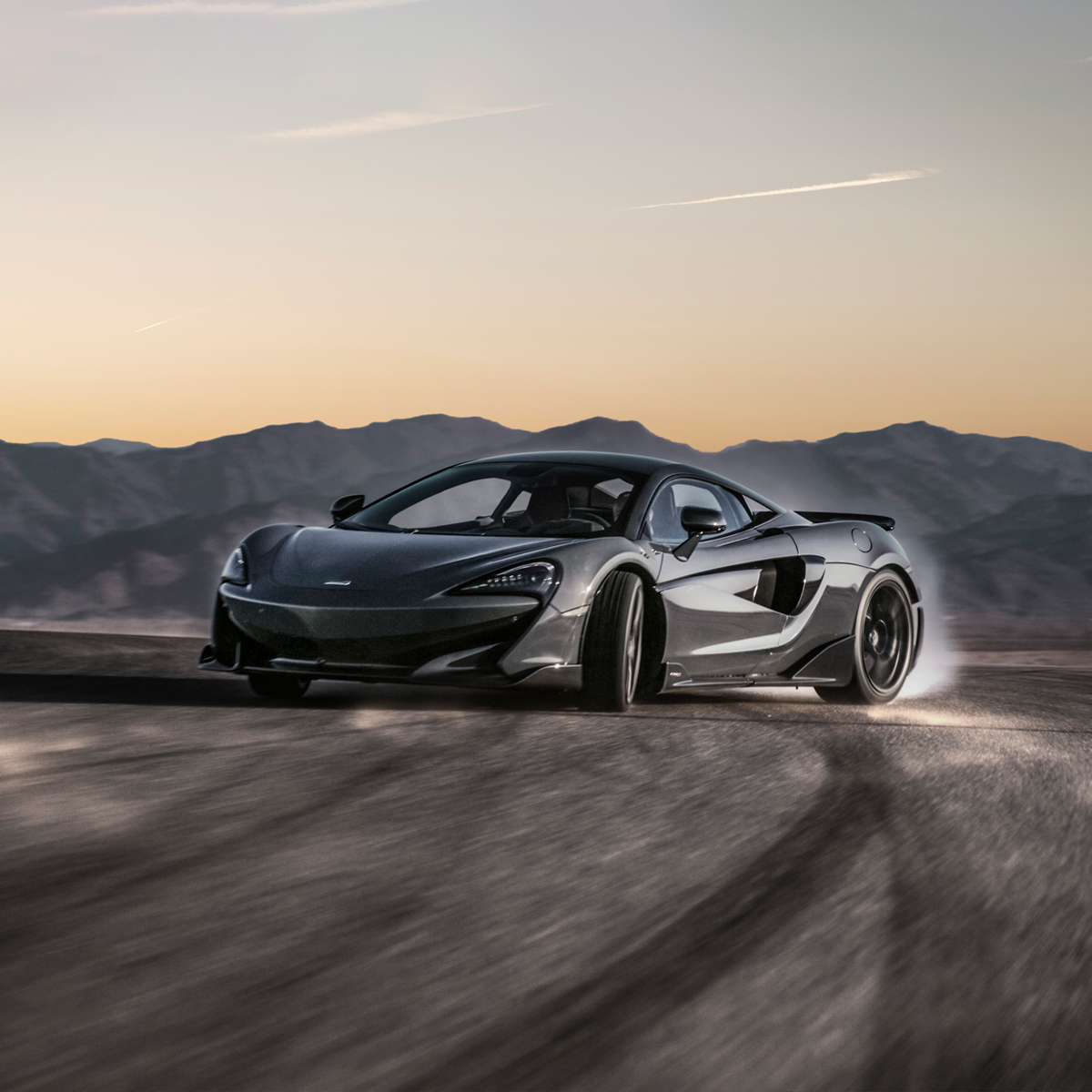 McLaren 600LT driving in a bend on tarmac at high speed. Blurry mountains can be seen in the background.