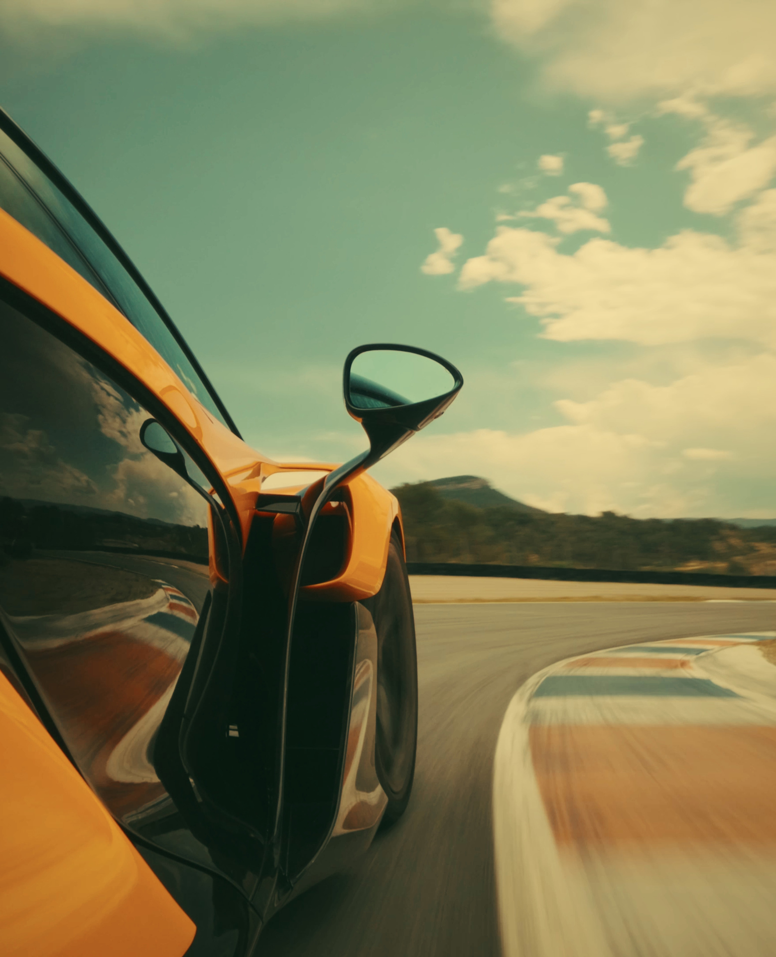 A low-angle dynamic shot of an orange and black McLaren W1 on a racetrack, captured from the rear-three-quarter view during a high-speed turn.
