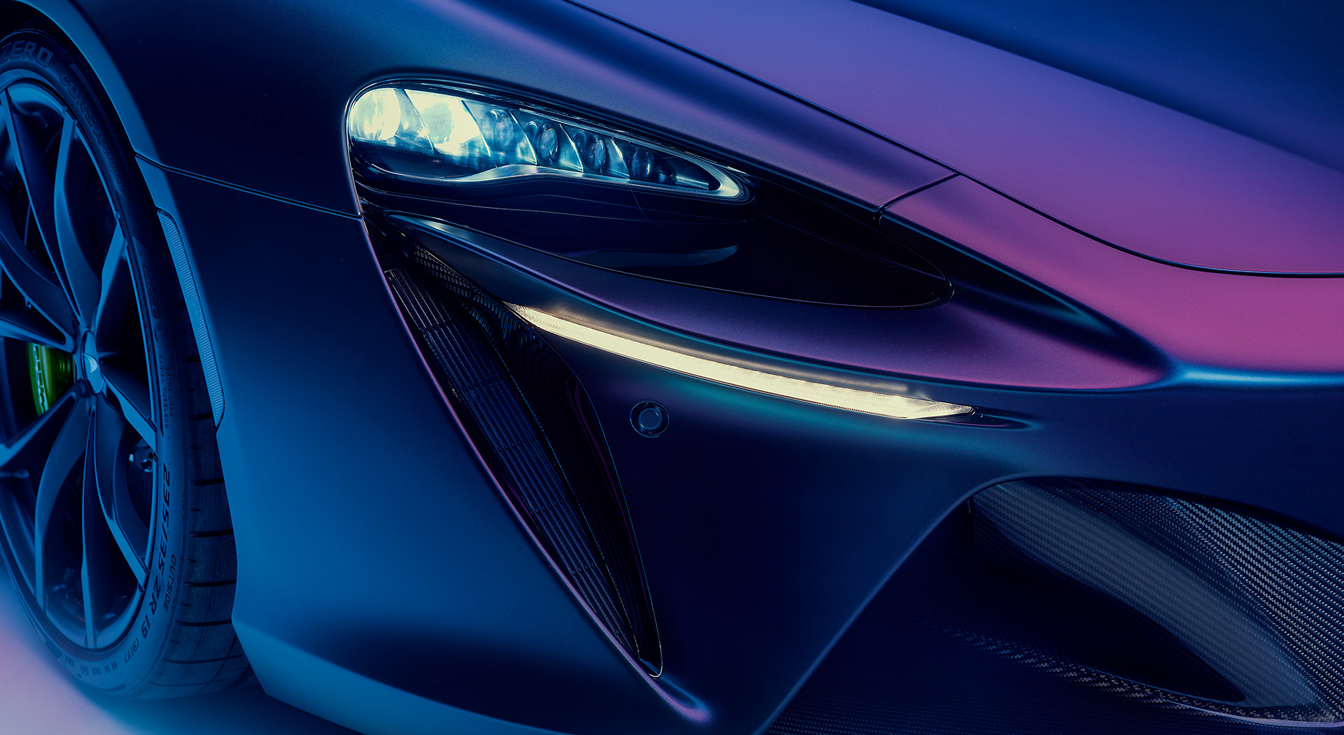 A close-up studio shot of a McLaren Artura's front quarter, highlighting its intricate LED headlights and a unique color-shifting blue and purple paint finish.