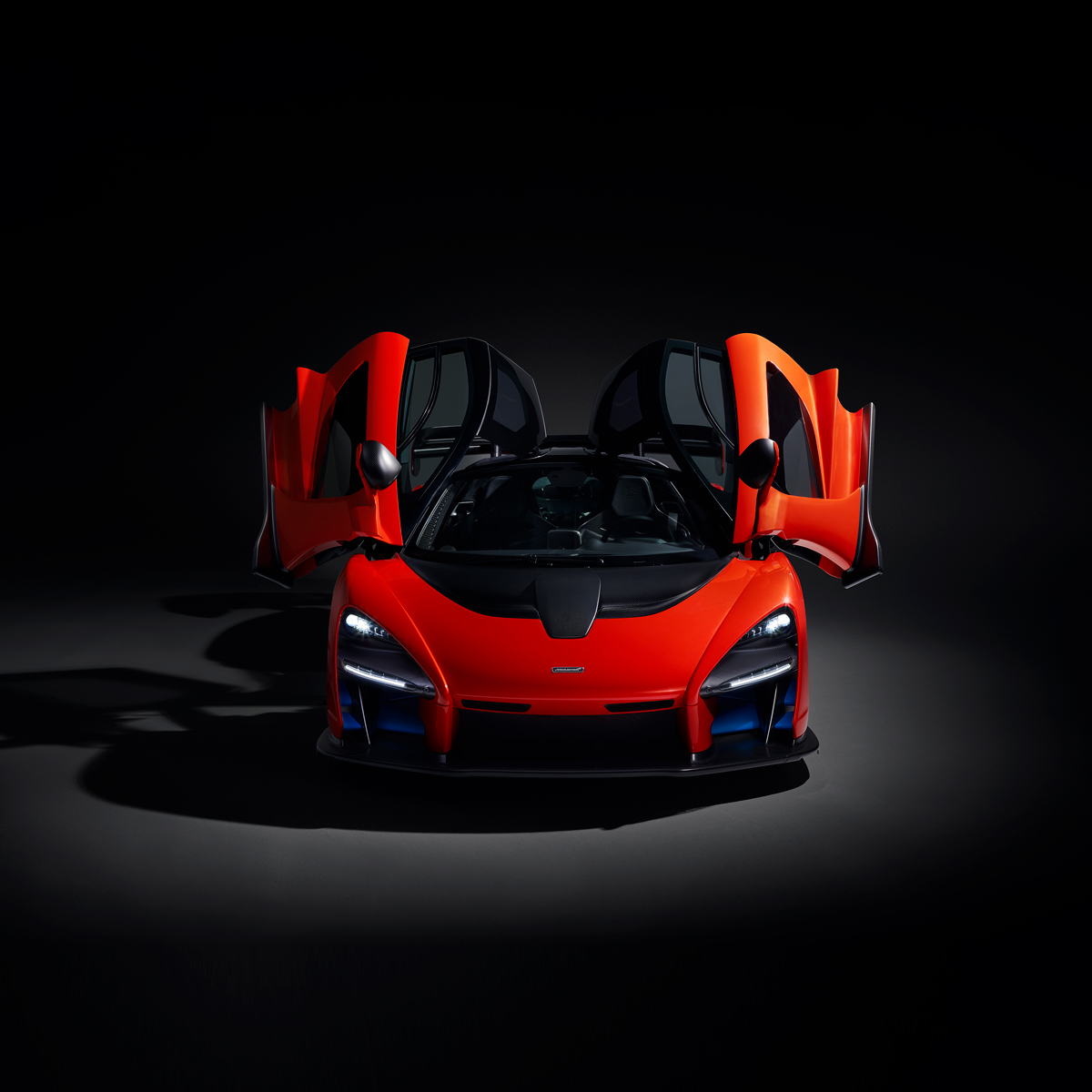 The red McLaren Senna photographed in a dark moody studio environment with the dihedral doors open.