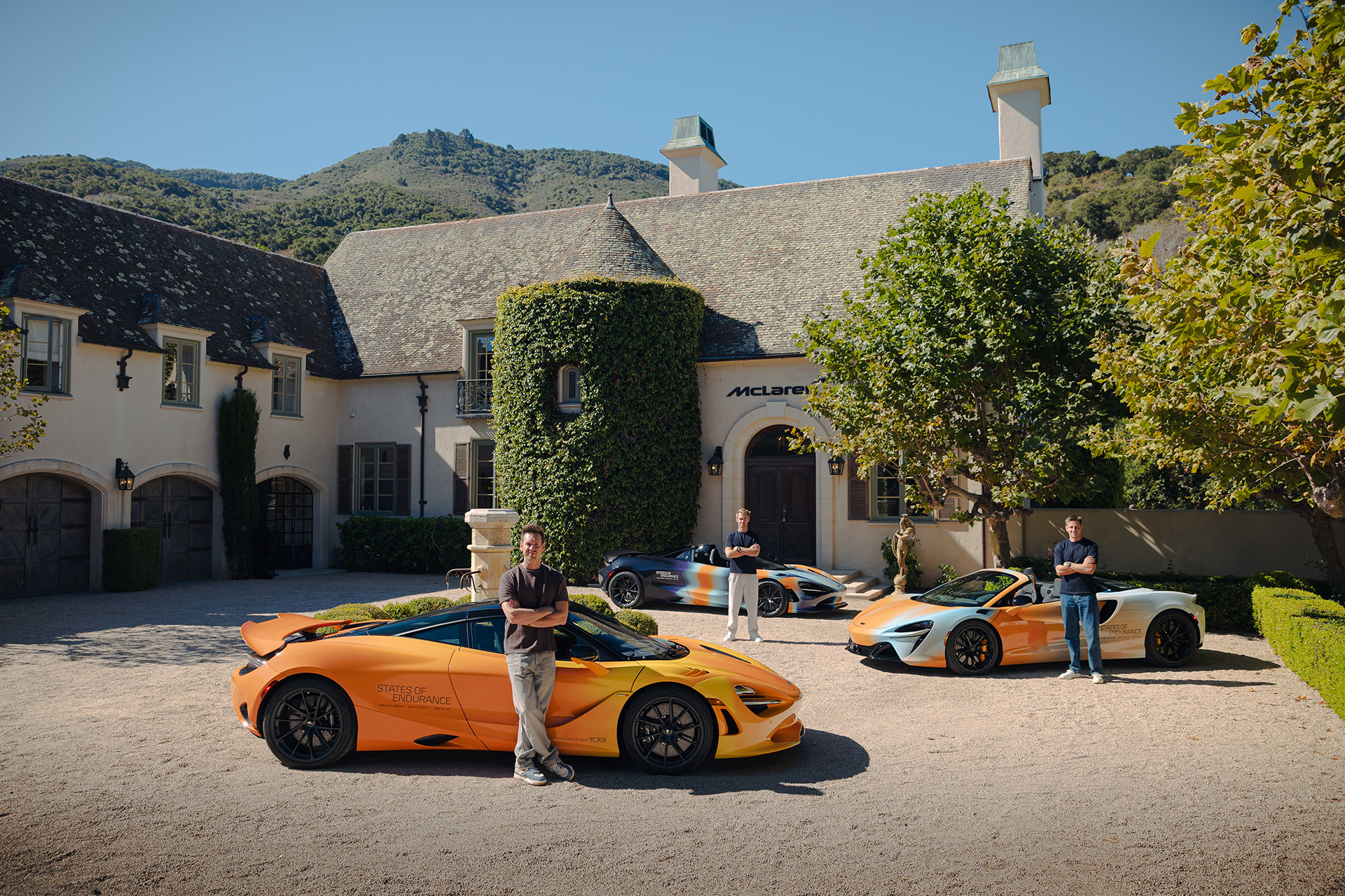 A group photo from the McLaren 'States of Endurance' campaign, showing three men posing with three custom-liveried supercars—an orange 720S and two Arturas—in front of a grand building.