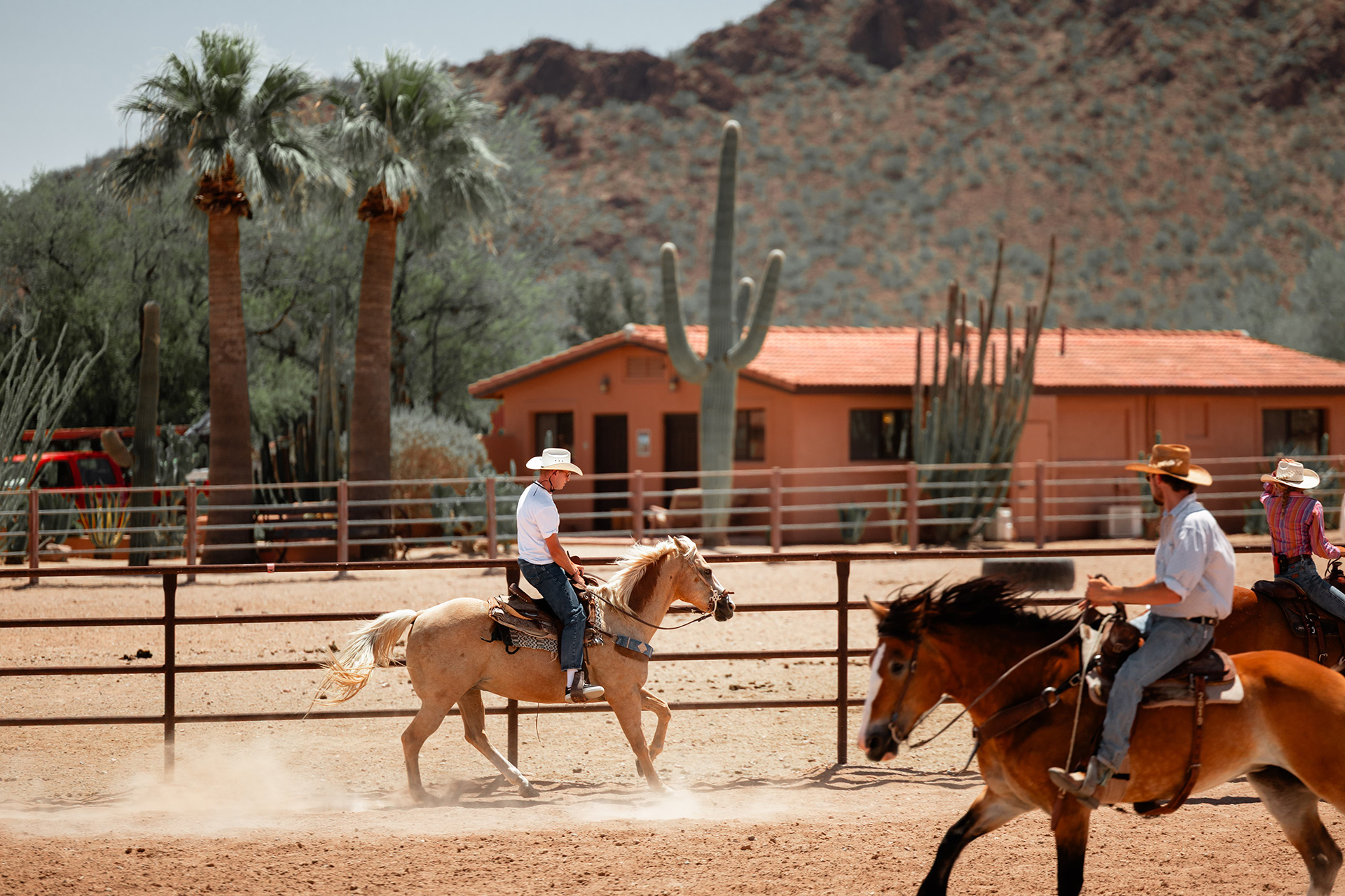 Two people are riding horses at a ranch in a sunny desert landscape, a scene from Day 4 of the 'McLaren States of Endurance' road trip.