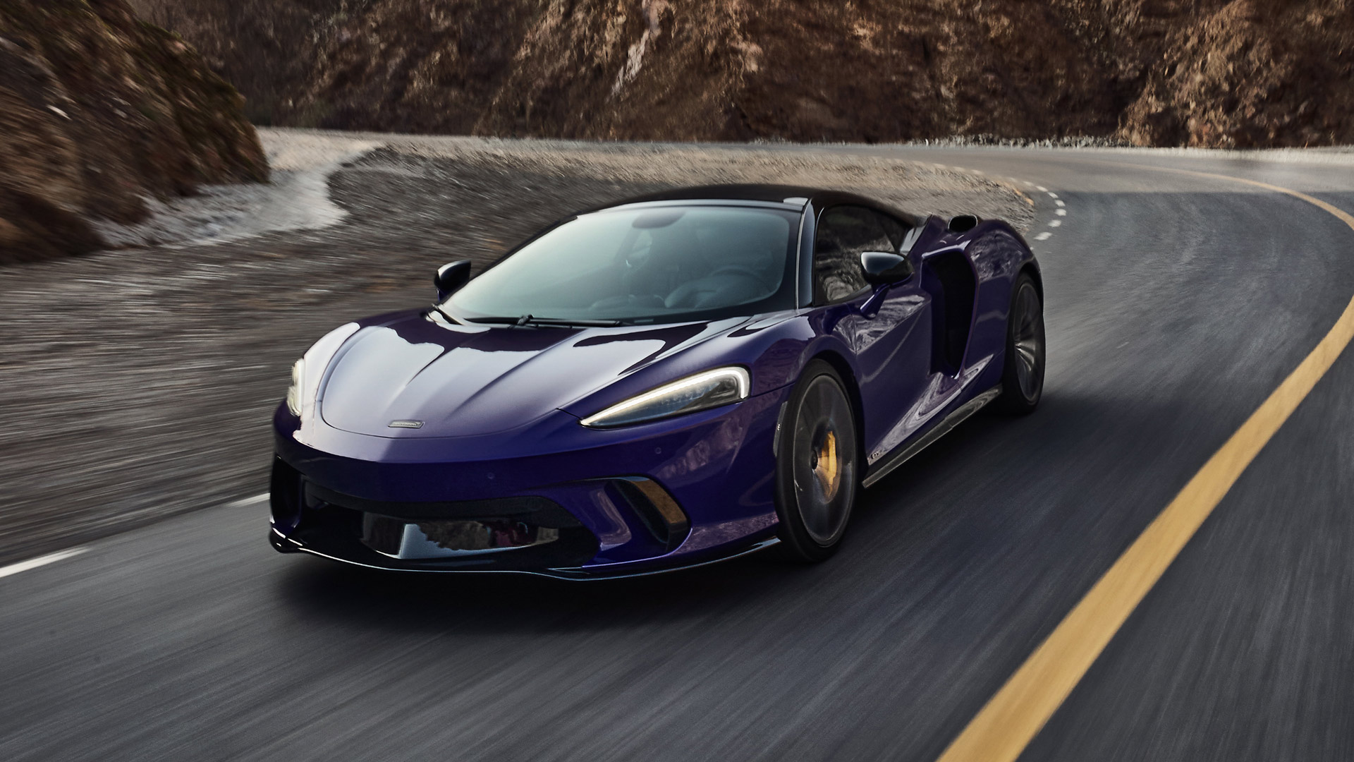 he purple McLaren Artura, a hybrid supercar, driving quickly on a scenic mountain road, showcasing its sleek design.