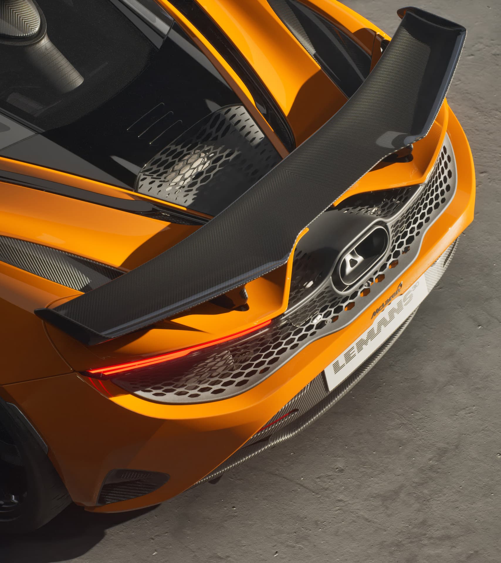 A close-up of the McLaren 720S Le Mans rear, highlighting its carbon fiber rear wing, exposed engine, and commemorative "Le Mans" badging.