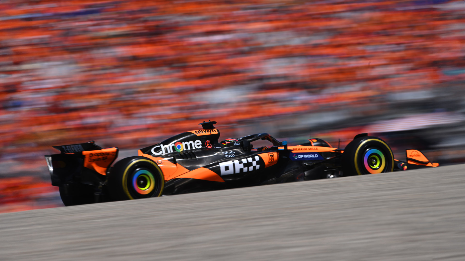 A side view of the McLaren MCL39 racing car in a high-speed motion shot, with the crowd and background blurred.