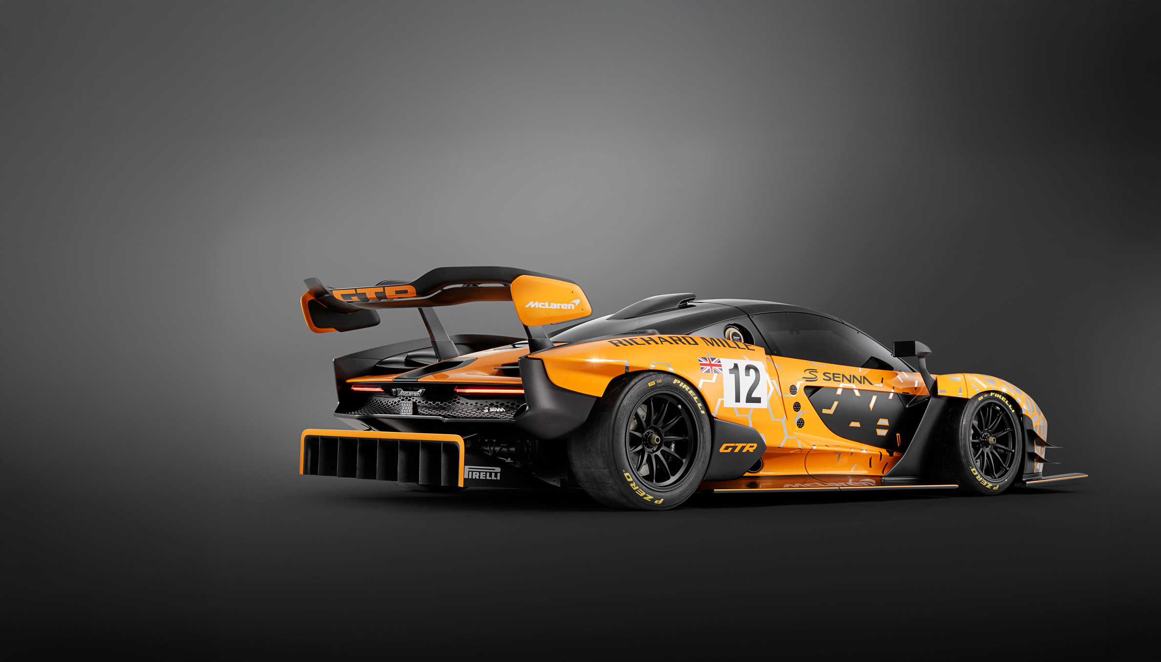 Rear side view of the orange and black McLaren Senna GTR concept car, photographed in a dark studio environment.
