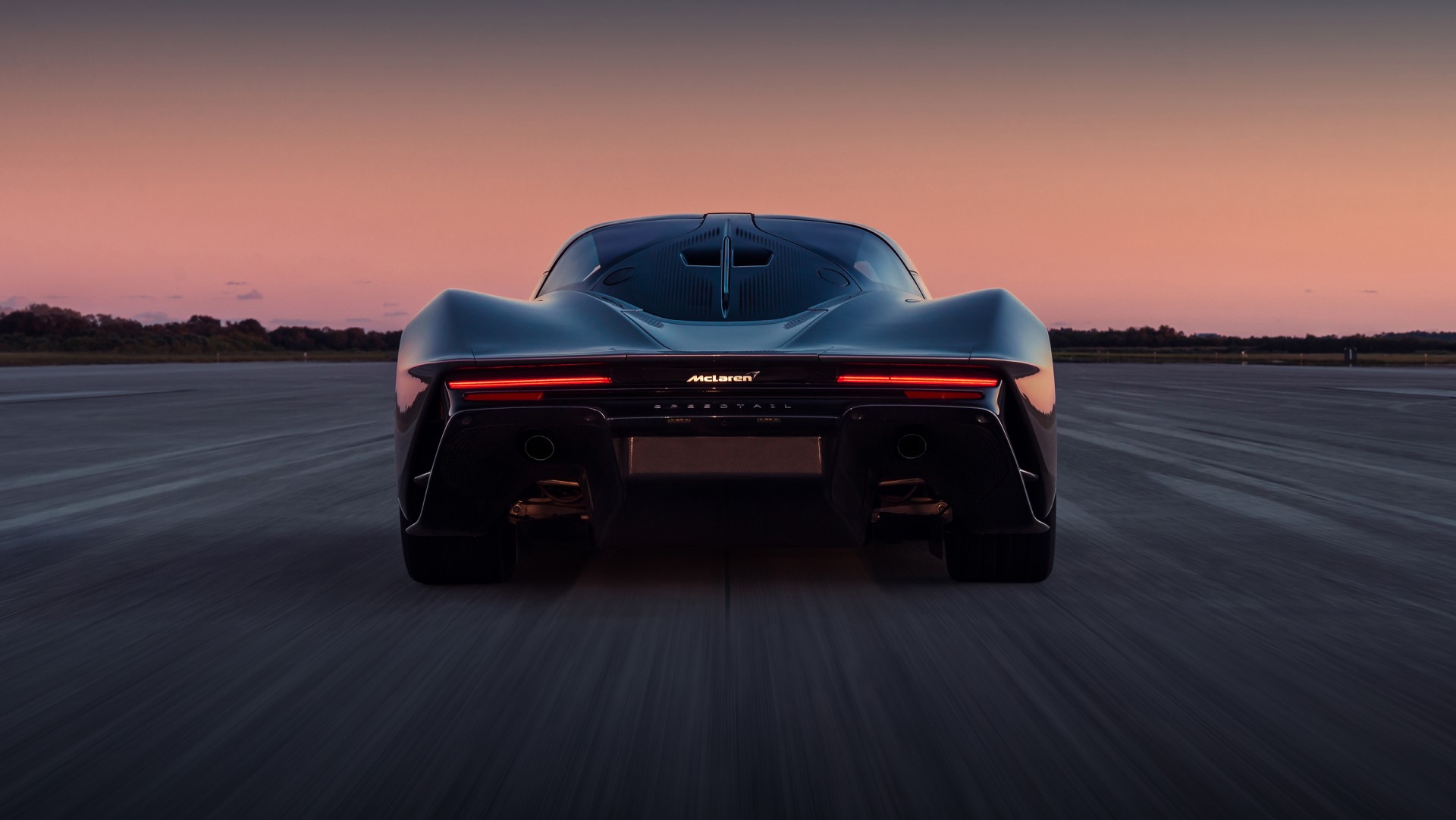 The McLaren Speedtail's rear, showcasing its minimalist tail lights and exhaust outlets on an airstrip during a beautiful sunrise or sunset.