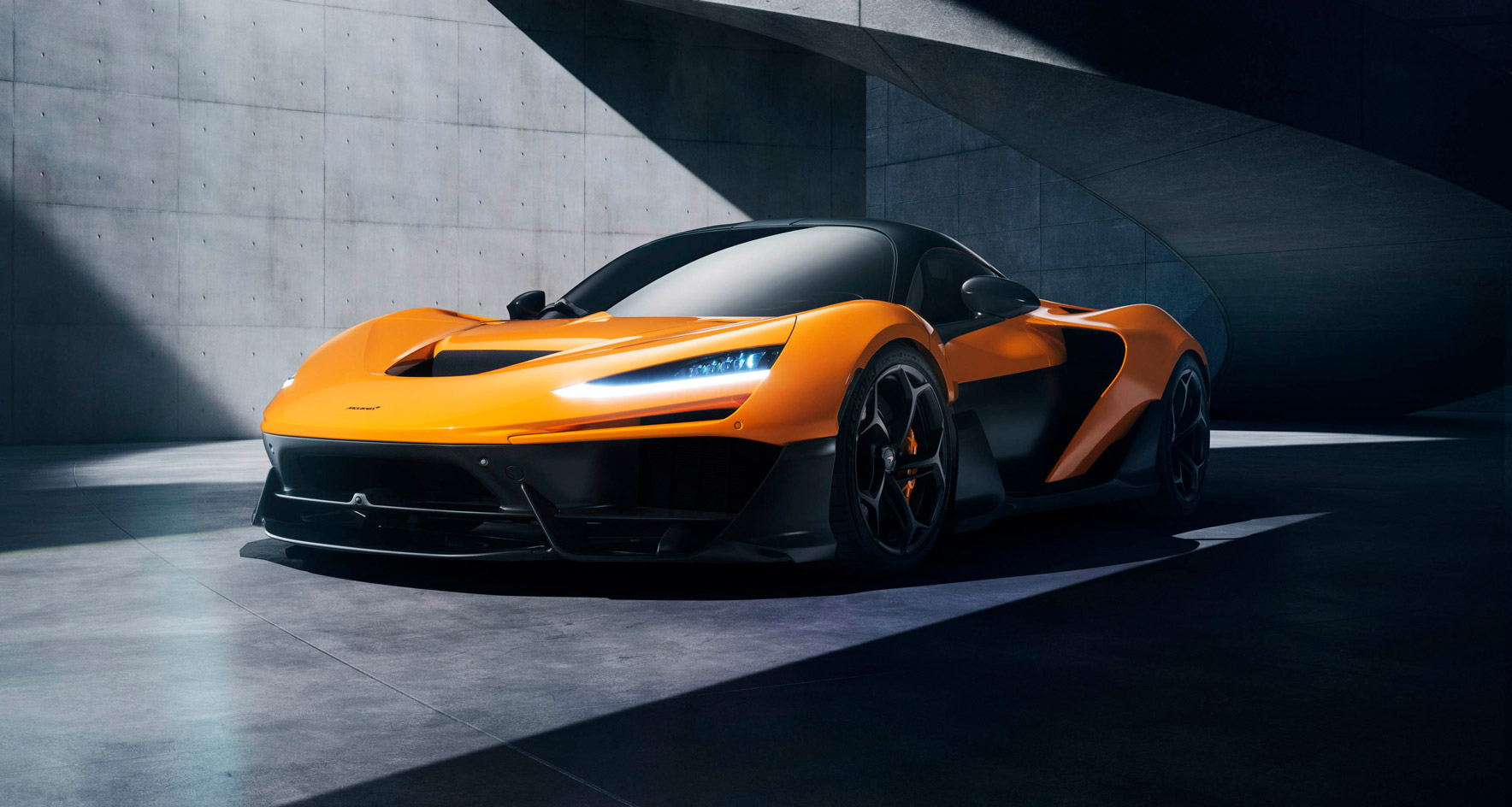 The McLaren W1 hypercar showcased in a banner image, highlighting its powerful front design and sleek headlights in a modern architectural setting.