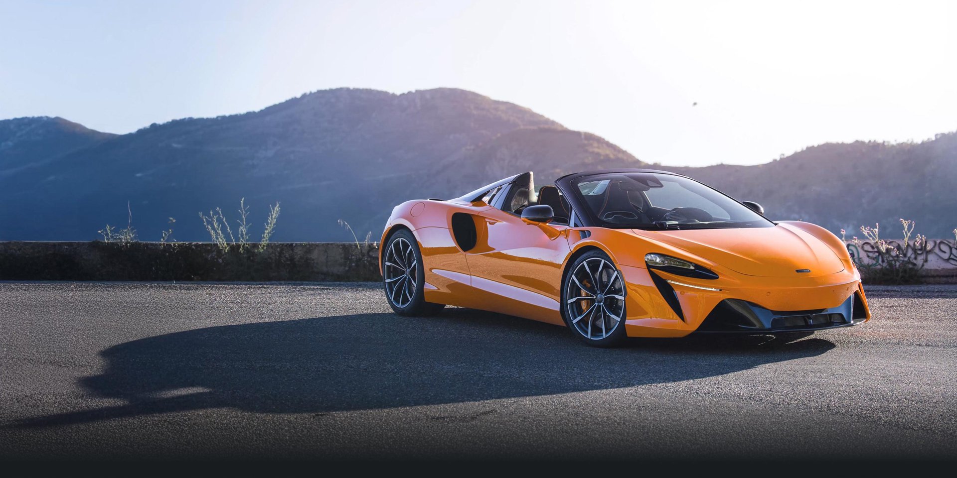 Orange McLaren Artura Spider parked on a mountain road.