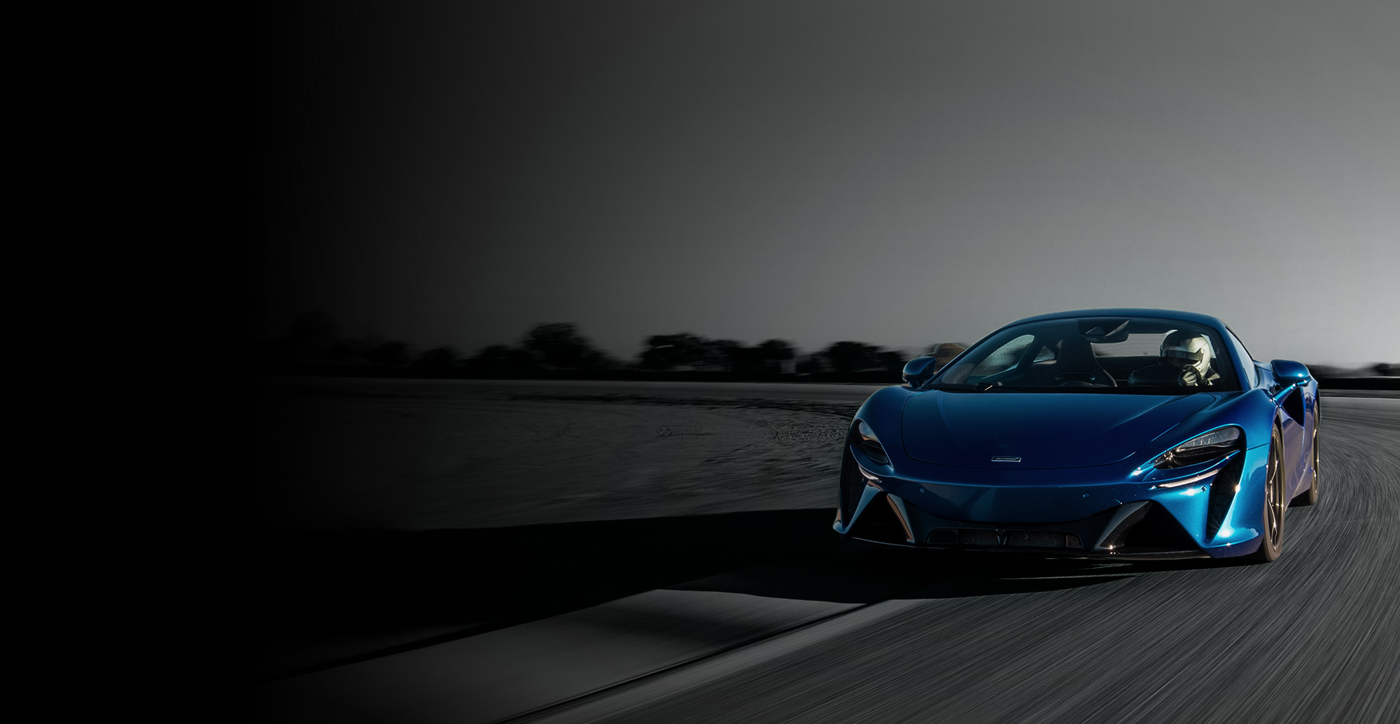 The McLaren Artura driving at speed on a track, with motion blur.