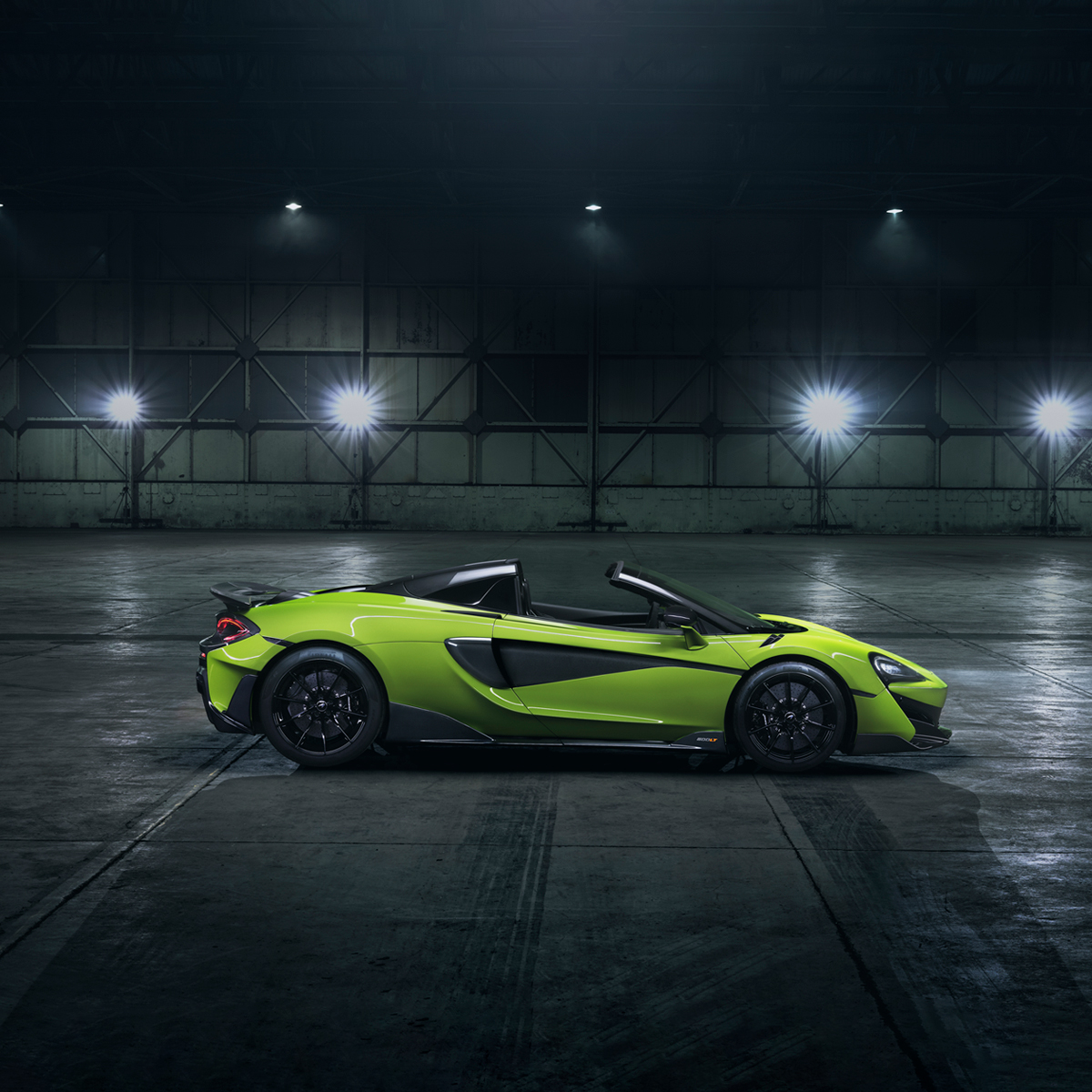 Side view of a bright green McLaren 600LT Spider, parked in a dark warehouse