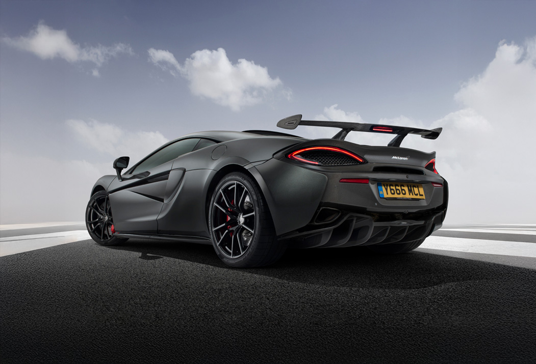  A grey McLaren 600LT supercar with a large rear wing, seen from the back, on a road with a cloudy sky.