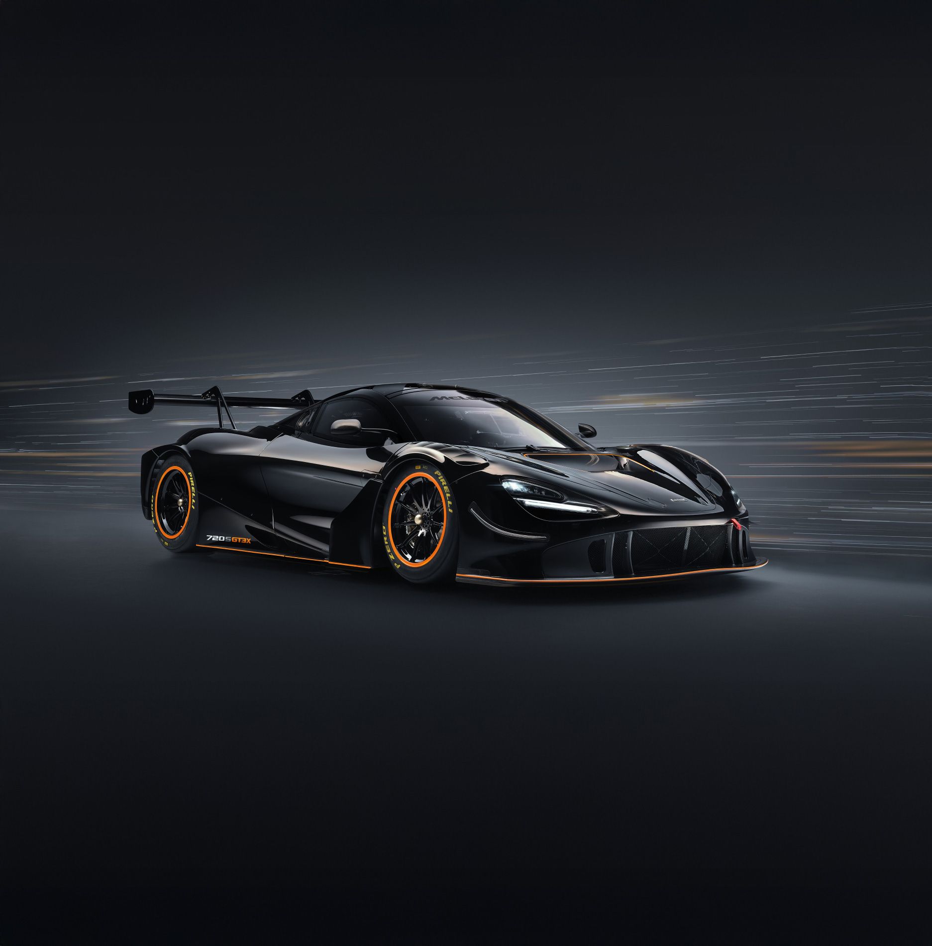 Black McLaren 720S GT3 X with orange detailing on a dark, blurry background.