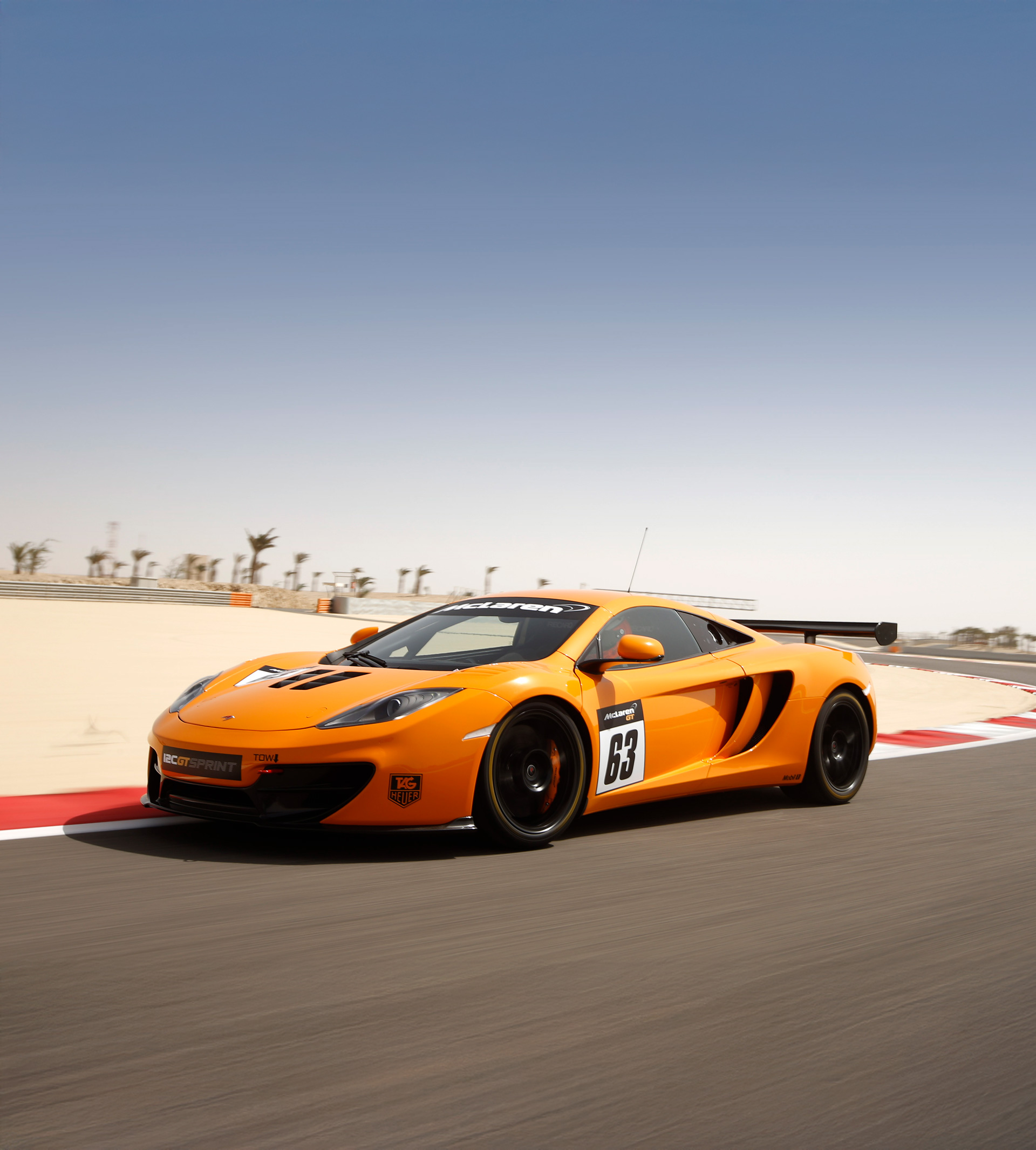 Orange McLaren 12C GT SPRINT driving around a race track on a sunny day. 