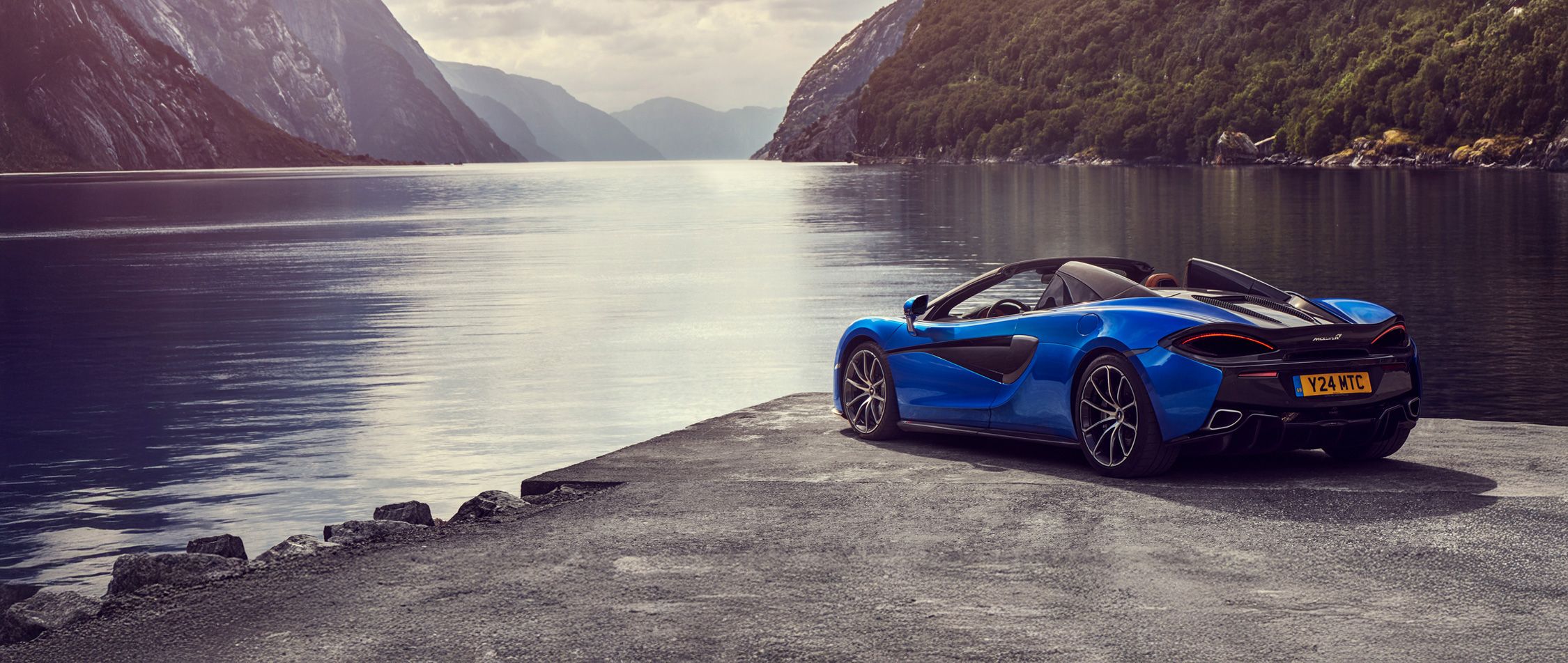 Blue McLaren parked on a rock, overlooking a lake.
