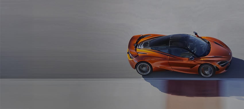 Orange McLaren 750S driving at speed down a tack.