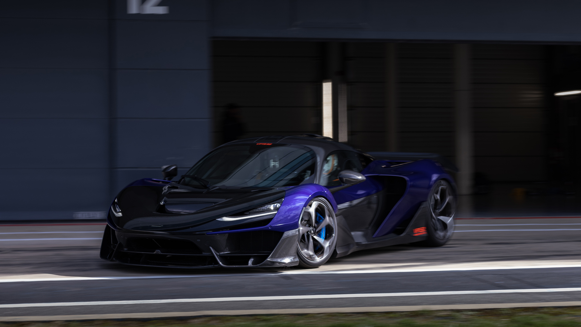 A three quarter shot of the front of a McLaren W1 slowly exiting the pit lane of the Silverstone track.