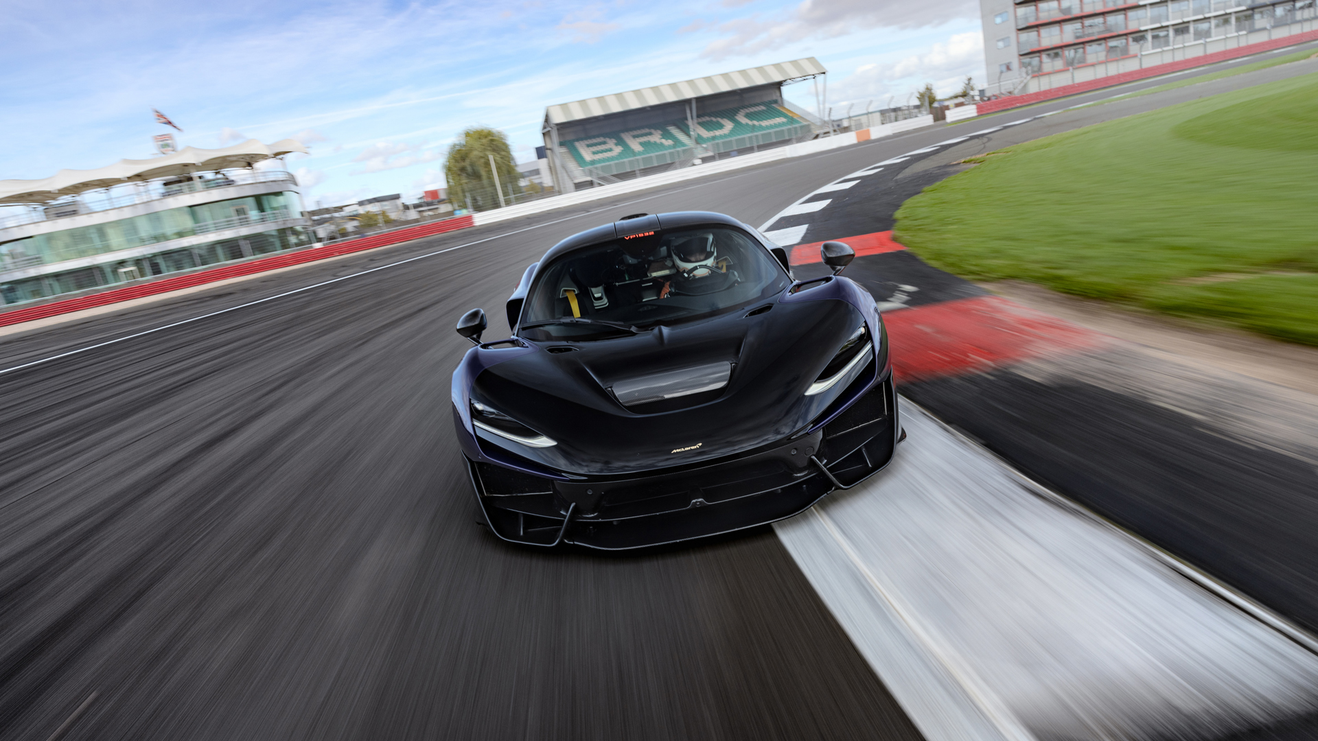 A shot of the front of a McLaren W1 prototype in royal blue driving at speed around a corner at the Silverstone track with motion blur to enhance the idea of speed.