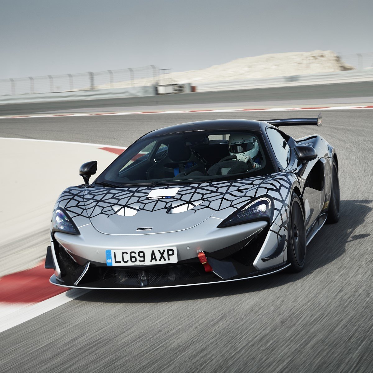 The McLaren 620R, a track-focused sports car, cornering on a circuit, highlighting its unique test livery and aerodynamic features.