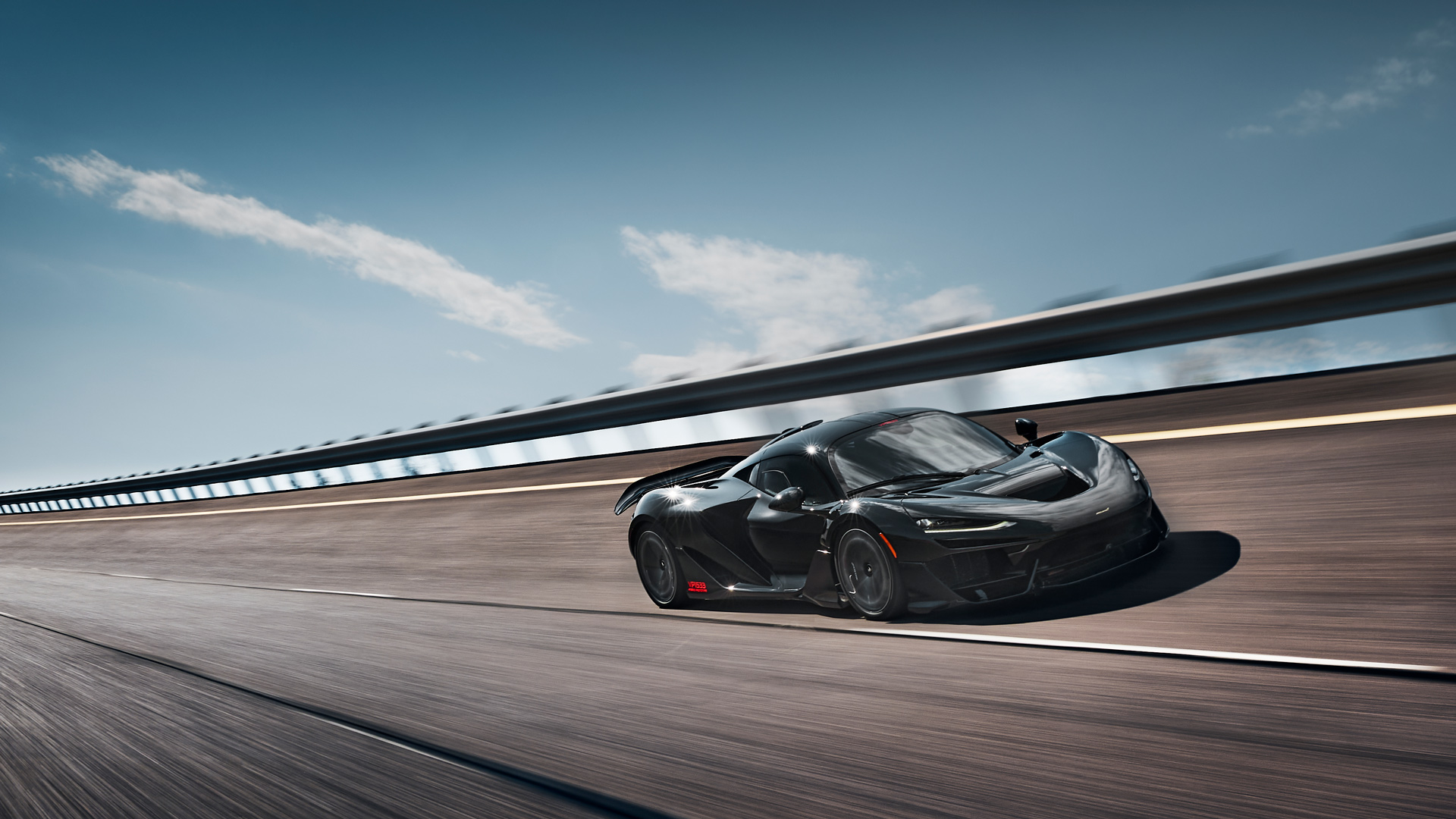 Black McLaren W1 prototype at speed on a highway in a hot, sunny environment. Low-angle shot emphasizing the car's speed, hybrid performance, and cooling system evaluation during desert durability testing.