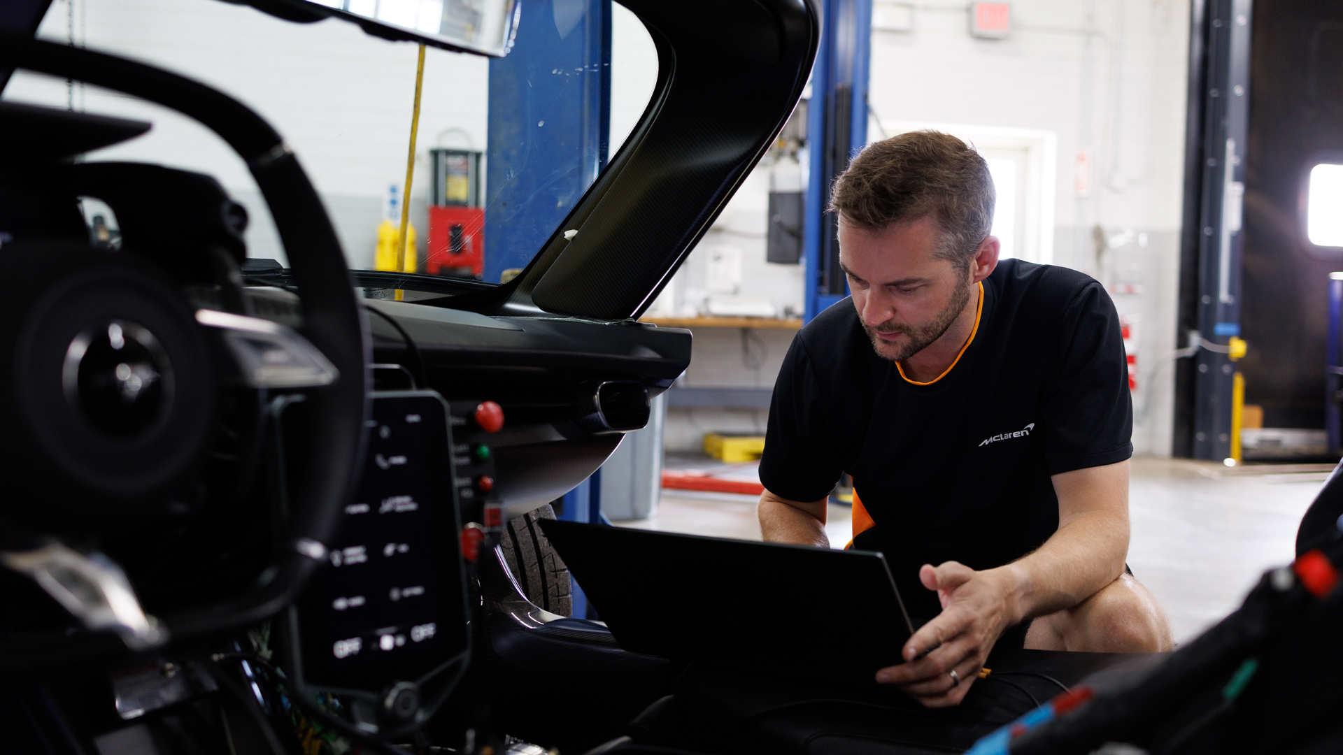 McLaren engineer performing a diagnostics check on the W1 hypercar prototype using a laptop inside the garage. Image highlights the technical complexity of the Ultimate Series hybrid powertrain and development testing process.