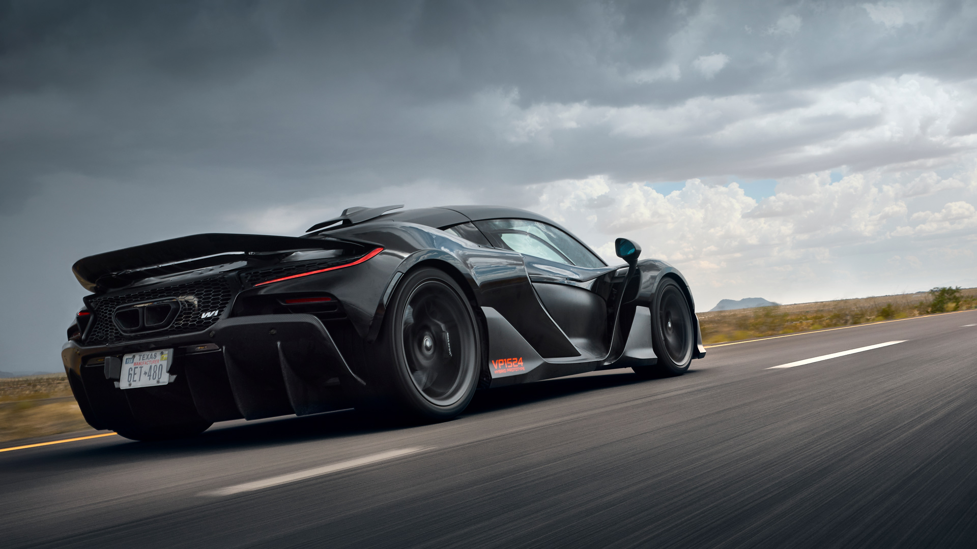 Aggressive rear three-quarter view of the McLaren W1 hypercar prototype with a Texas license plate and active rear wing deployed. The shot emphasizes the large rear diffuser and hot climate testing for cooling and high-speed stability.