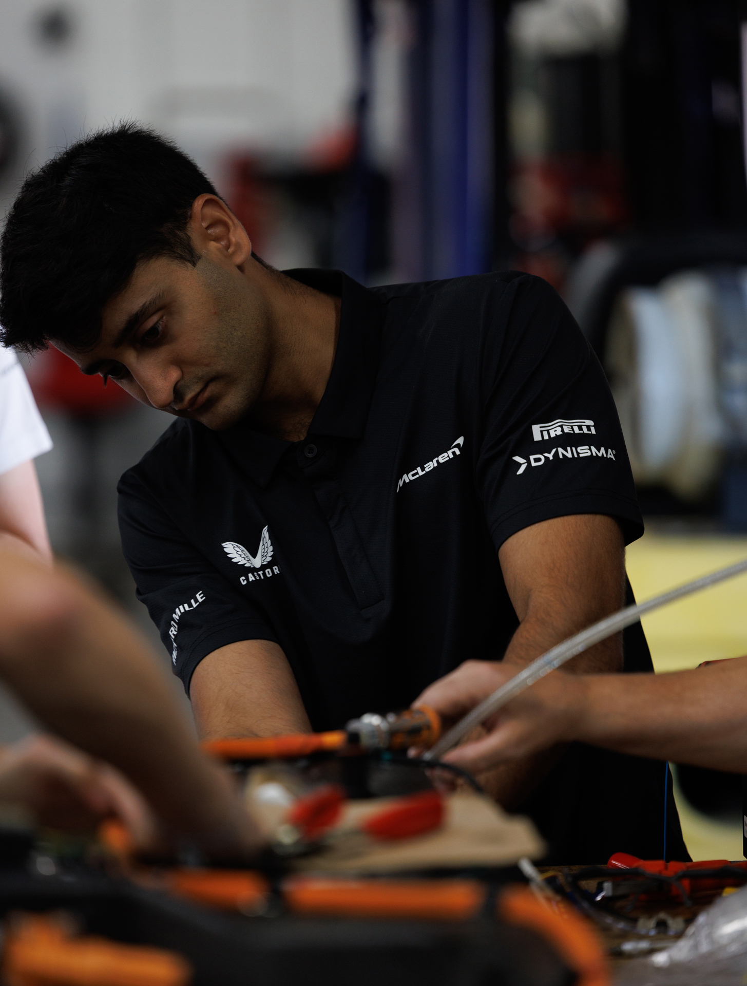 Close-up of Vikram Shah, a McLaren engineer, concentrating while working on the exposed electronics and components of the W1 hypercar prototype in a service garage. The focus is on the crucial development and diagnostics required for extreme hot weather validation.