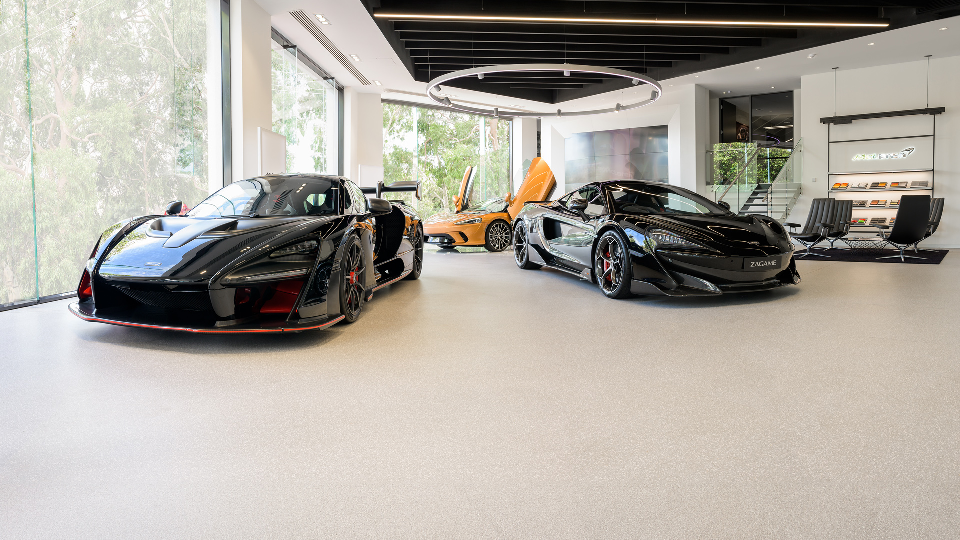 McLaren Adelaide showroom featuring three luxury supercars: a black McLaren Senna hypercar (left) and a black McLaren 720S (right) on display. In the background, an orange McLaren supercar shows its signature dihedral door open.