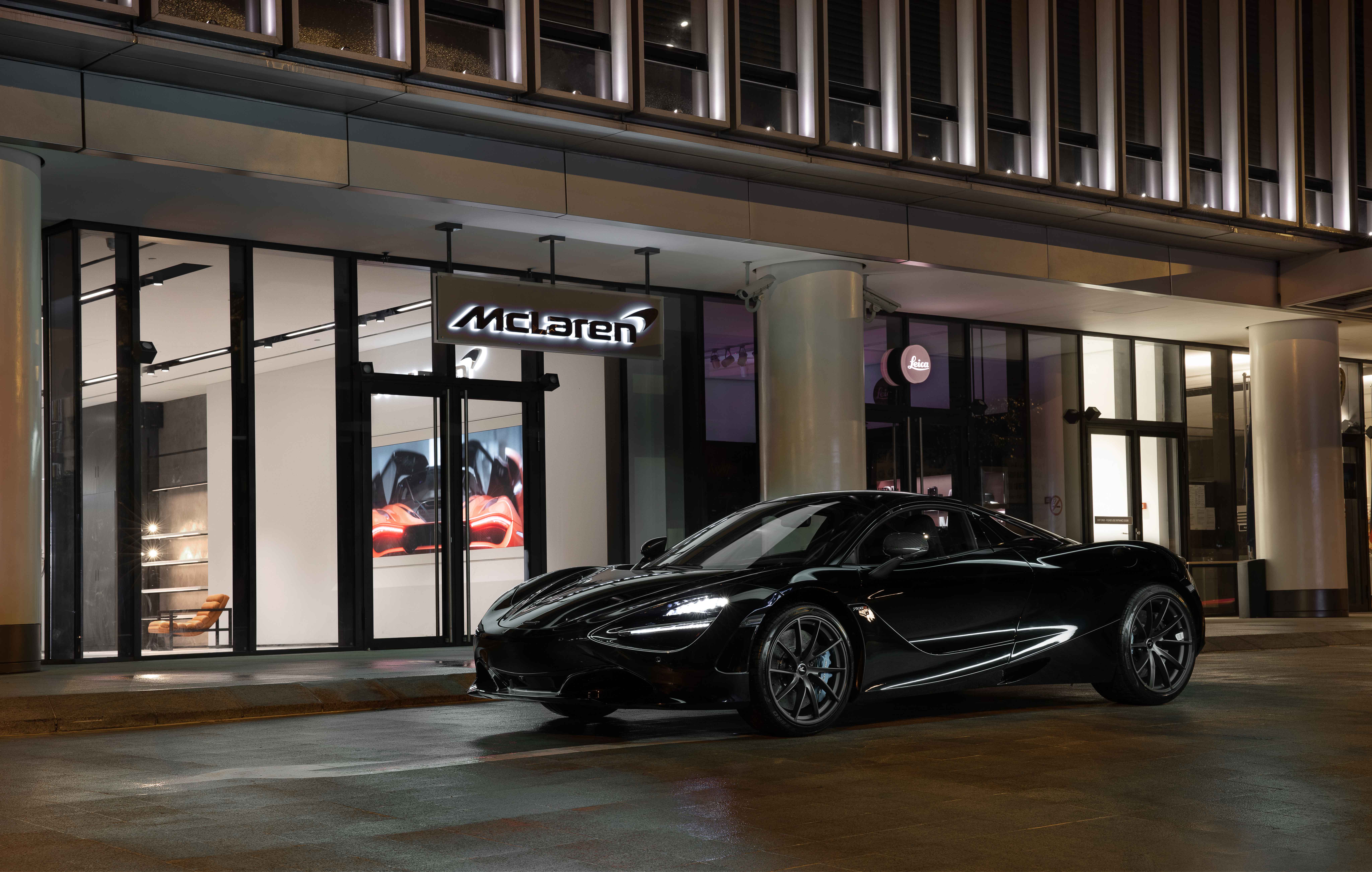 Black McLaren parked outside the Ho Chi Minh City McLaren retailer storefront at night. The store is lit up in the dark.