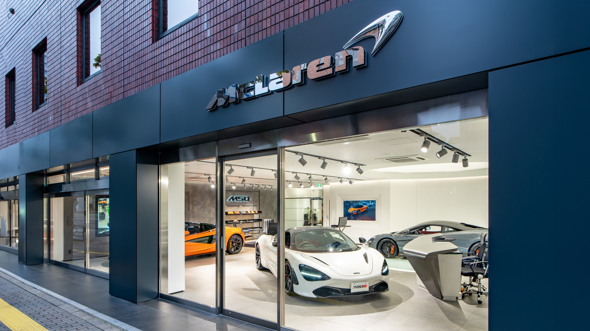 McLaren Azabu official retailer exterior in Minato, Tokyo, Japan. A white McLaren 720S supercar is displayed in the window, showcasing the dealership's modern design and a visible MSO (McLaren Special Operations) bespoke customization area.