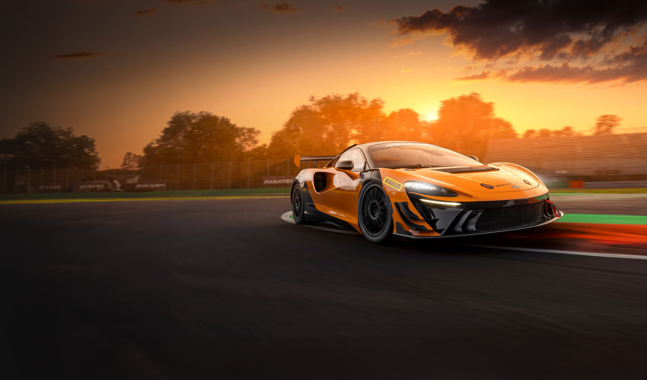 An orange McLaren Artura Trophy Evo race car on a racetrack at sunset.