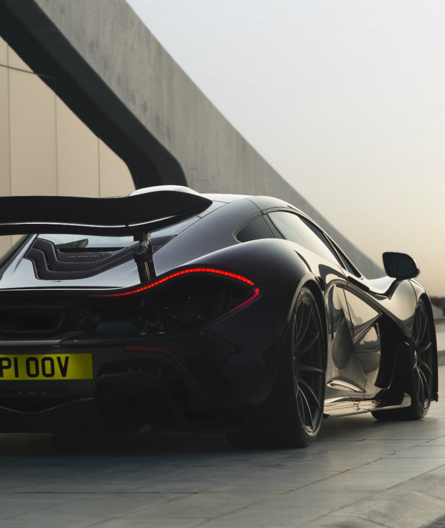 The rear of the McLaren P1 hypercar, with its tail lights glowing red in a dark, atmospheric setting.