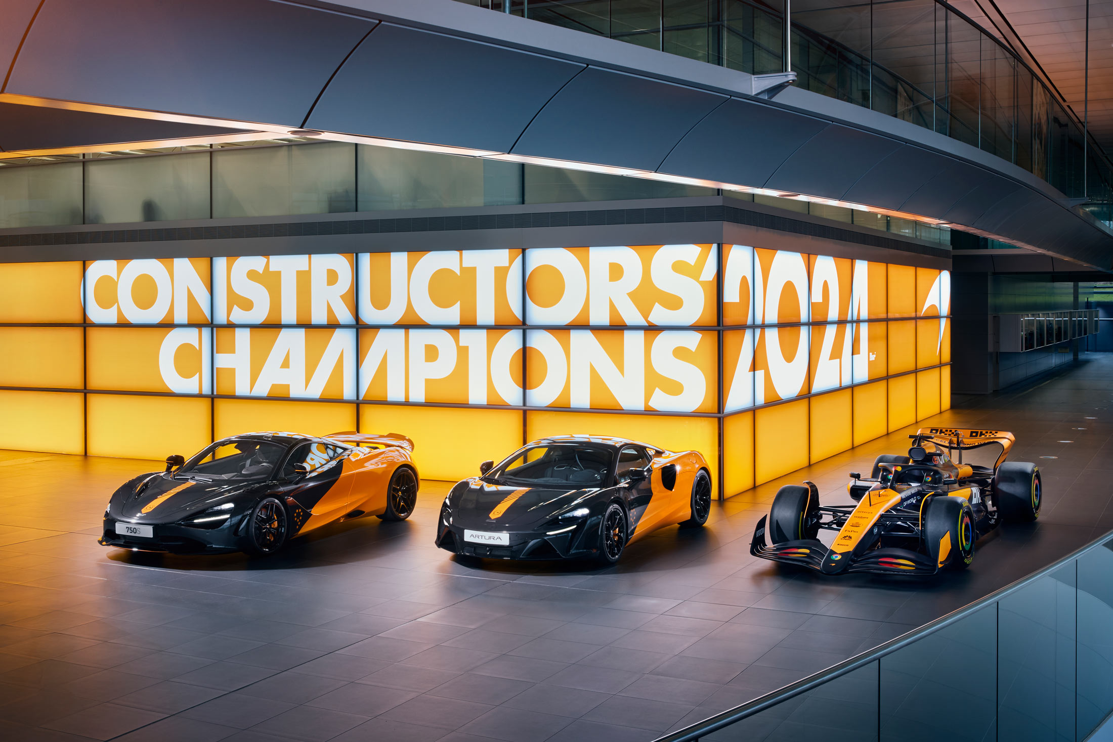 McLaren Constructors Livery. The 750s, Artura, and Formula 1 car all parked in a row, in front of a screen wall which reads Constructors' Champions 2024.