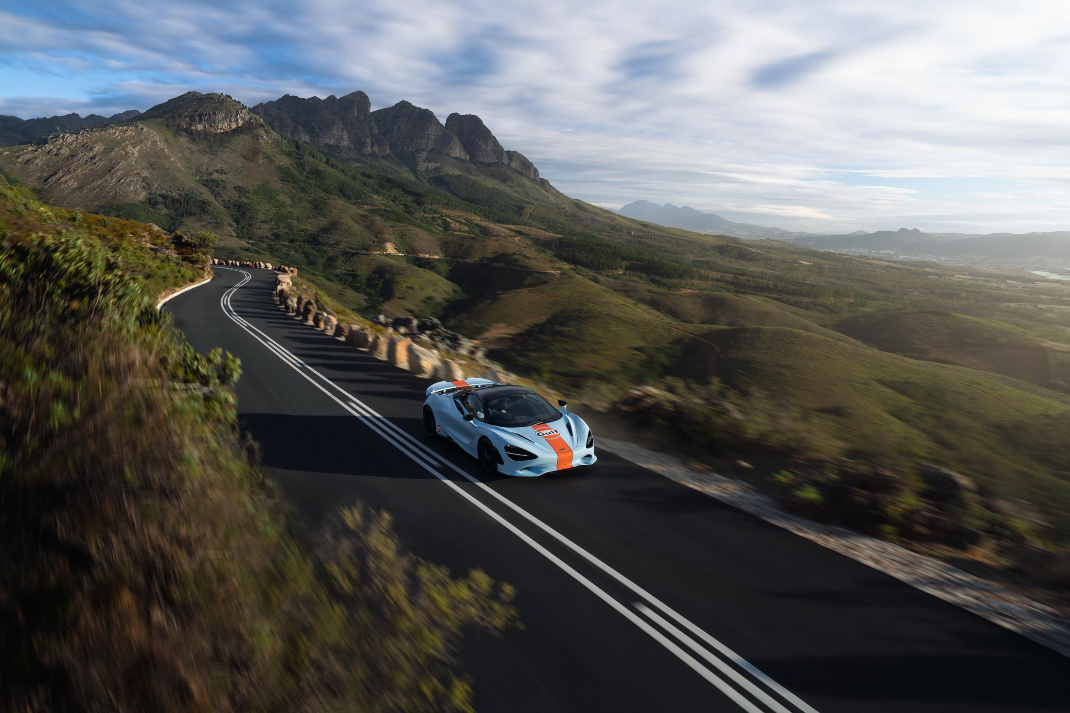 The Gulf Branded McLaren driving down a winding road in the hills.