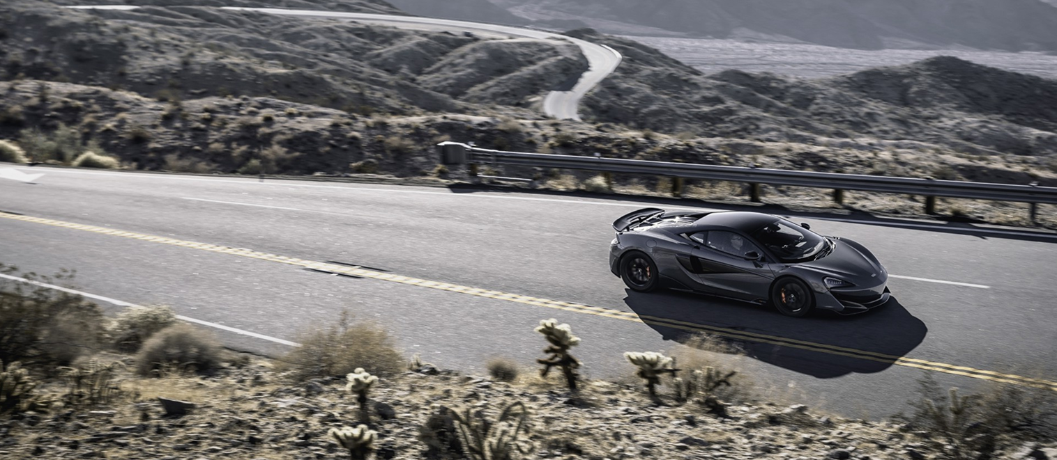 Dark grey McLaren supercar driving on a winding desert road, showcasing the performance and peace of mind provided by a McLaren extended warranty.