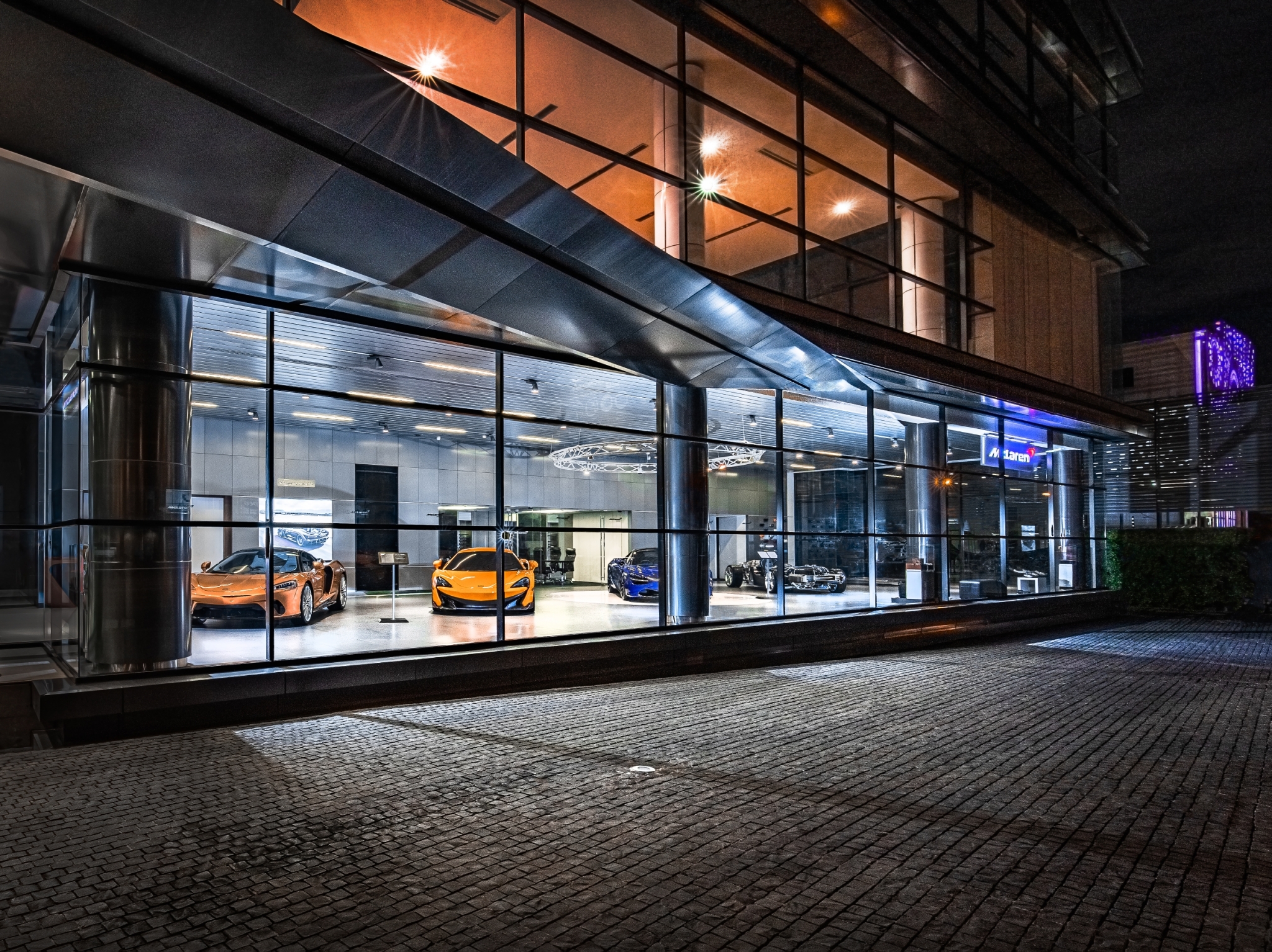 The McLaren Bangkok storefront lit up at night. A series of McLaren cars can be seen inside.