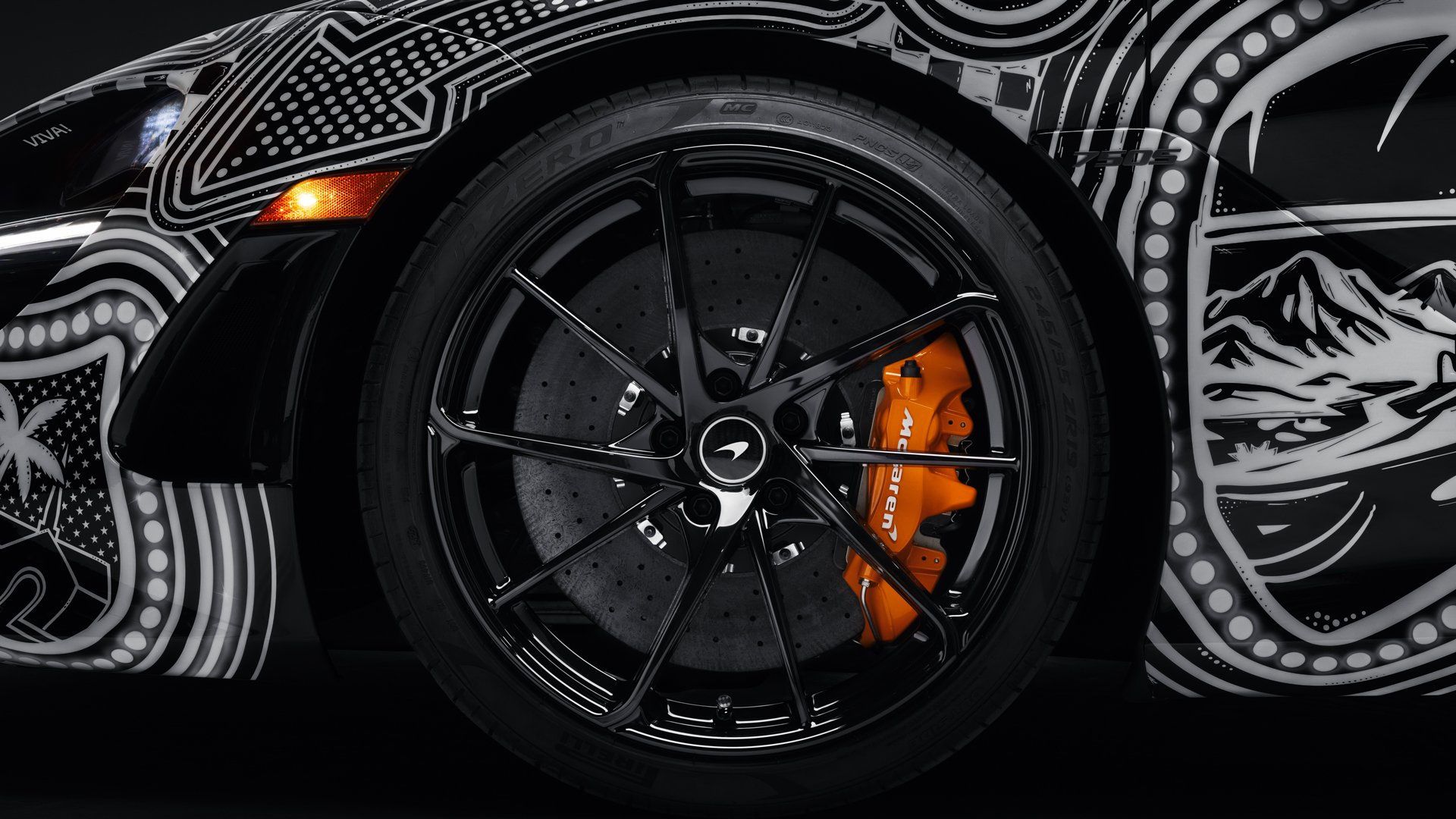 Close-up of the black alloy wheel and carbon ceramic brake system on the McLaren 750S, highlighted by a bright McLaren orange brake caliper, contrasting with the Project Viva livery.