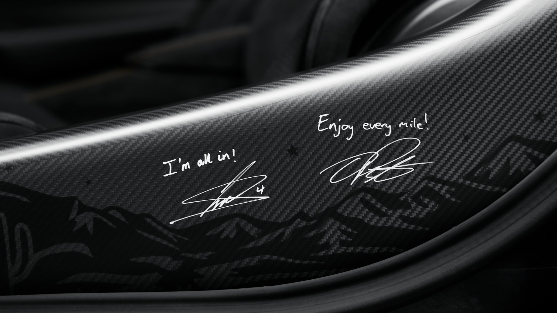 Close-up of the custom carbon fibre interior trim on the McLaren 750S MSO featuring engraved signatures from McLaren F1 drivers Lando Norris and Oscar Piastri, reading 'I'm all in!' and 'Enjoy every mile!'.