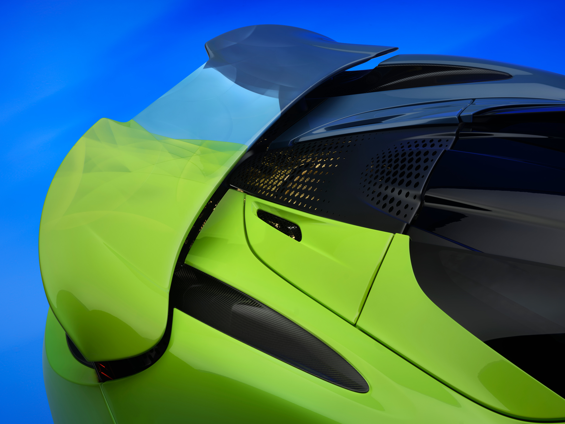 The rear wing of the Project Chromology 750s by MSO and Nat Bowen, on display against a glowing blue background. The car is various overlaying shades of green and blue and can be seen parked at an angle with its headlights on.