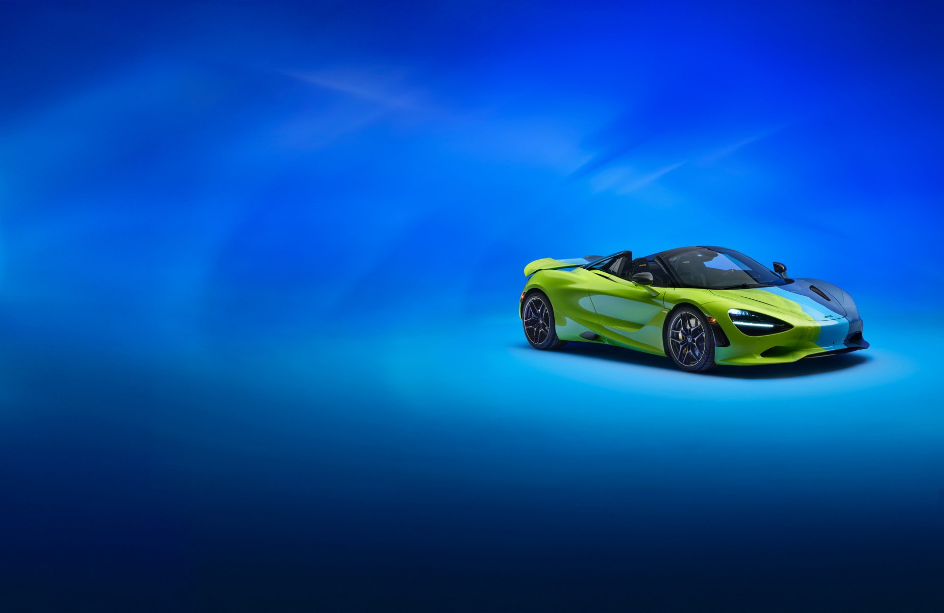 The Project Chromology 750s by MSO and Nat Bowen, on display against a glowing blue background. The car is various overlaying shades of green and blue and can be seen parked at an angle with its headlights on.
