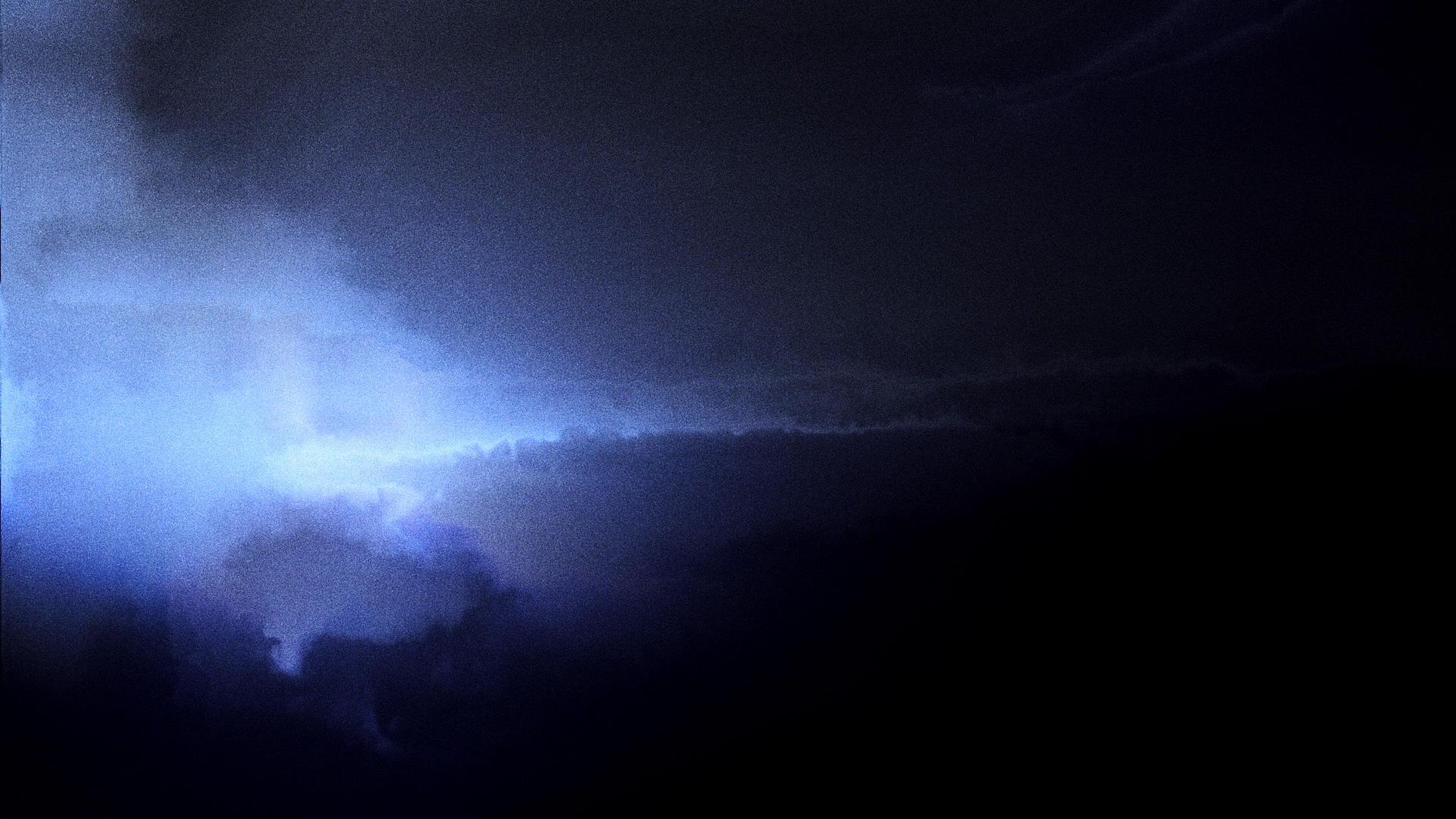 A grainy shot of dark thunder clouds with light piercing through the left hand side.