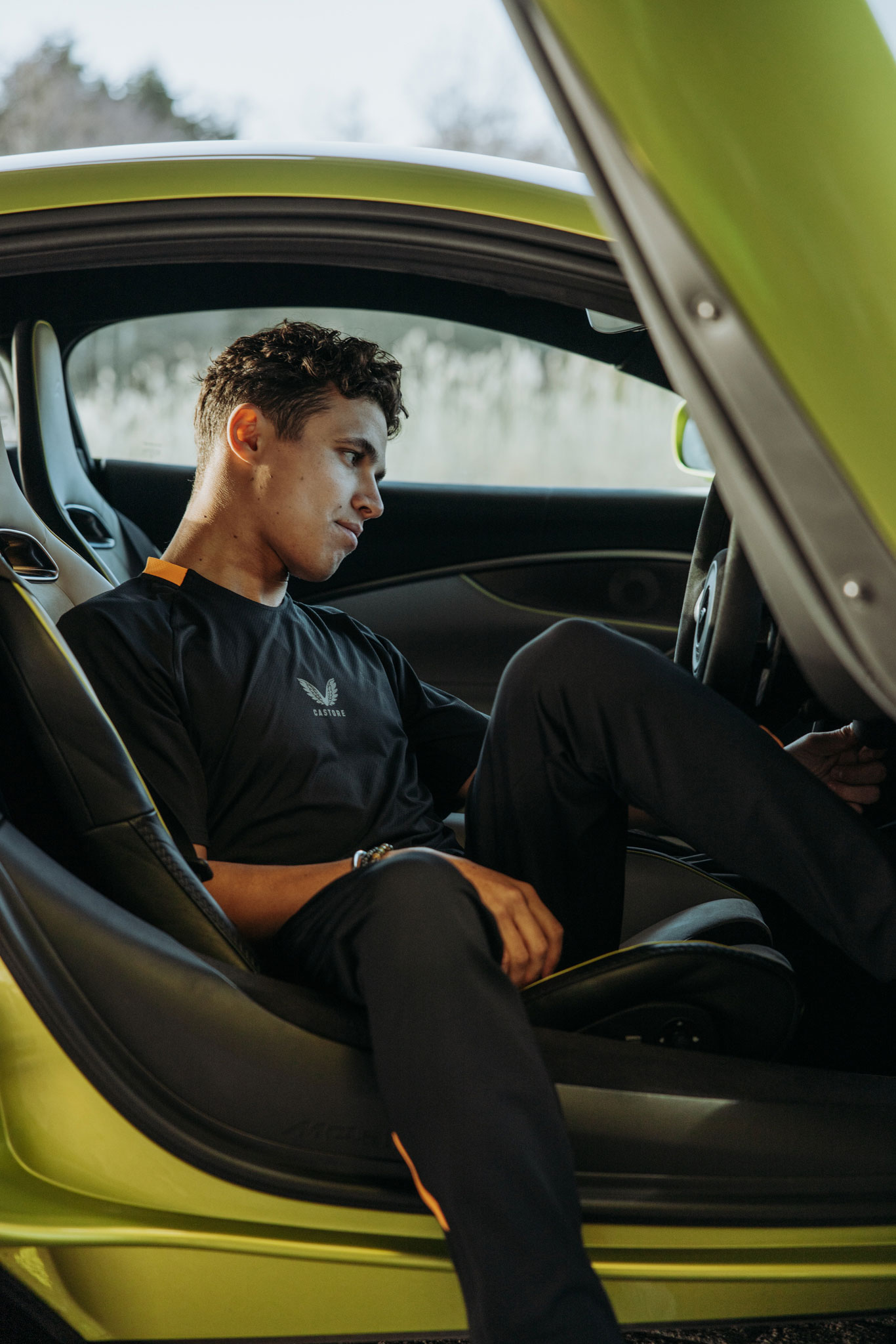 Lando Norris wearing McLaren Castore clothing while sat in a bright green McLaren car.