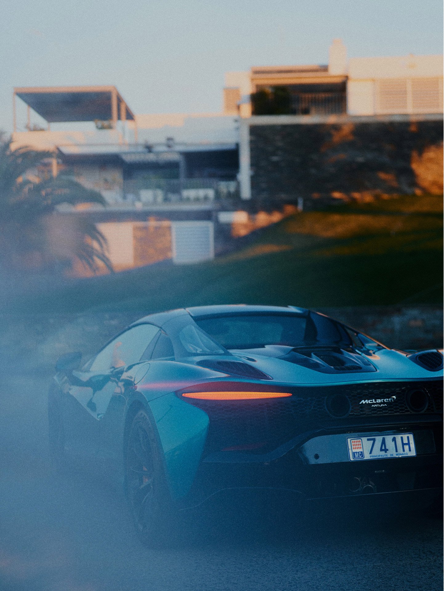 A low Rear view shot of the McLaren Artura Spider parked outside a luxury modern home.