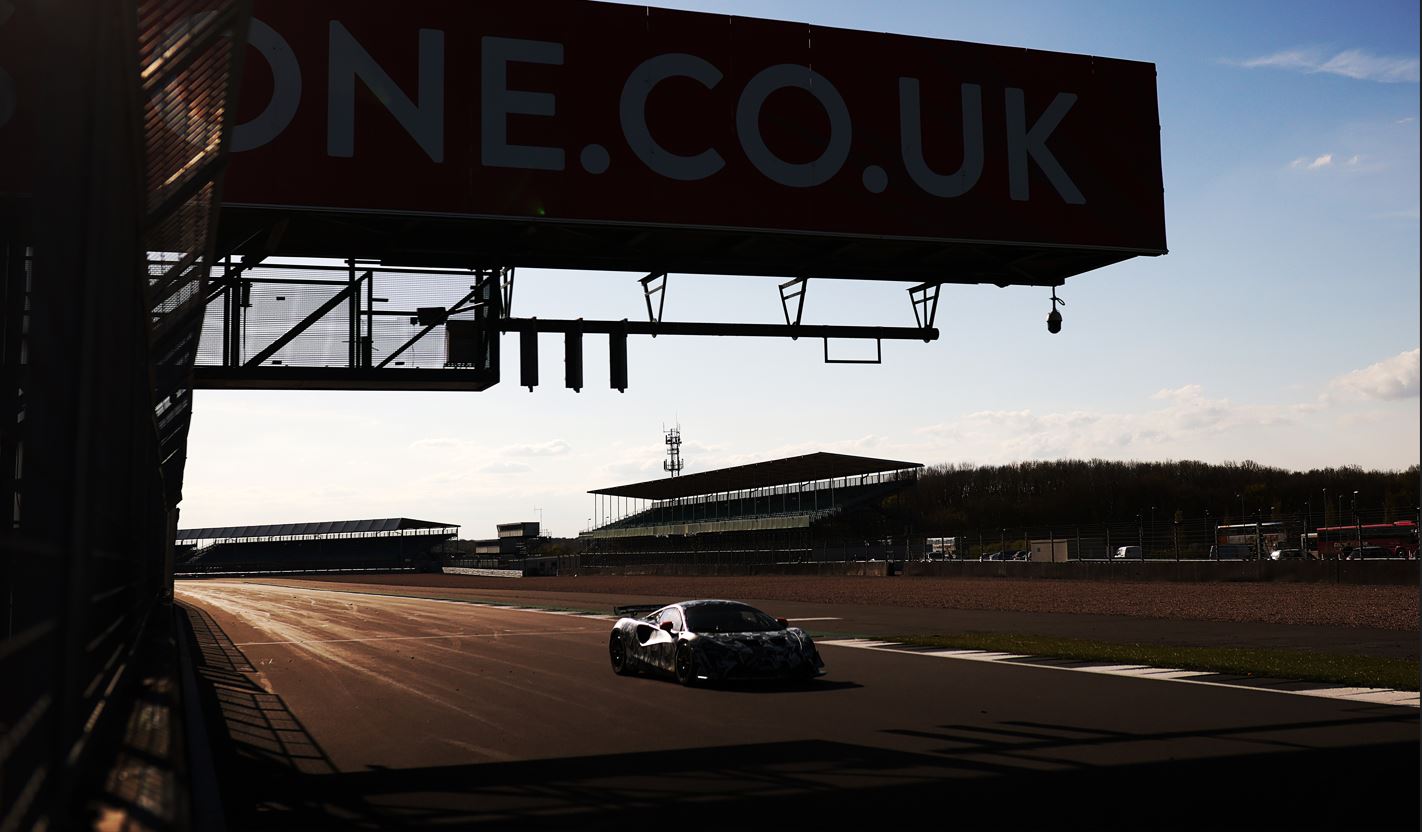 A McLaren Artura GT4 parked at the start line of a race track, with morning light behind it.