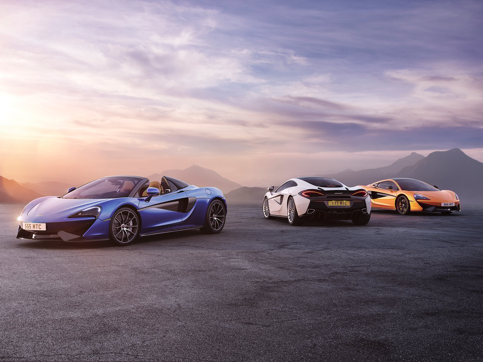Three McLaren vehicles parked on a mountain road, facing different directions. 